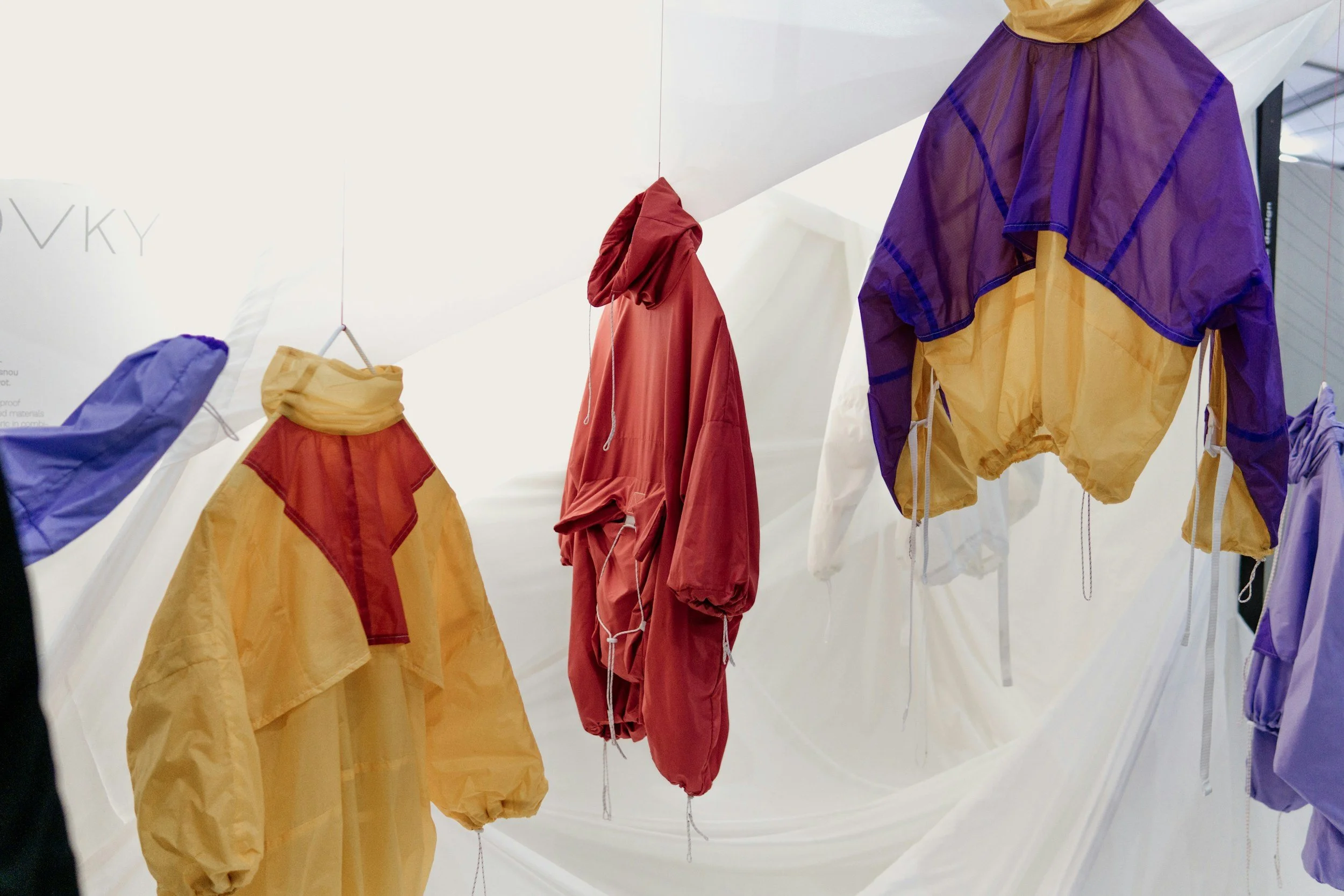 Colorful windbreaker jackets hanging from the ceiling in a display.