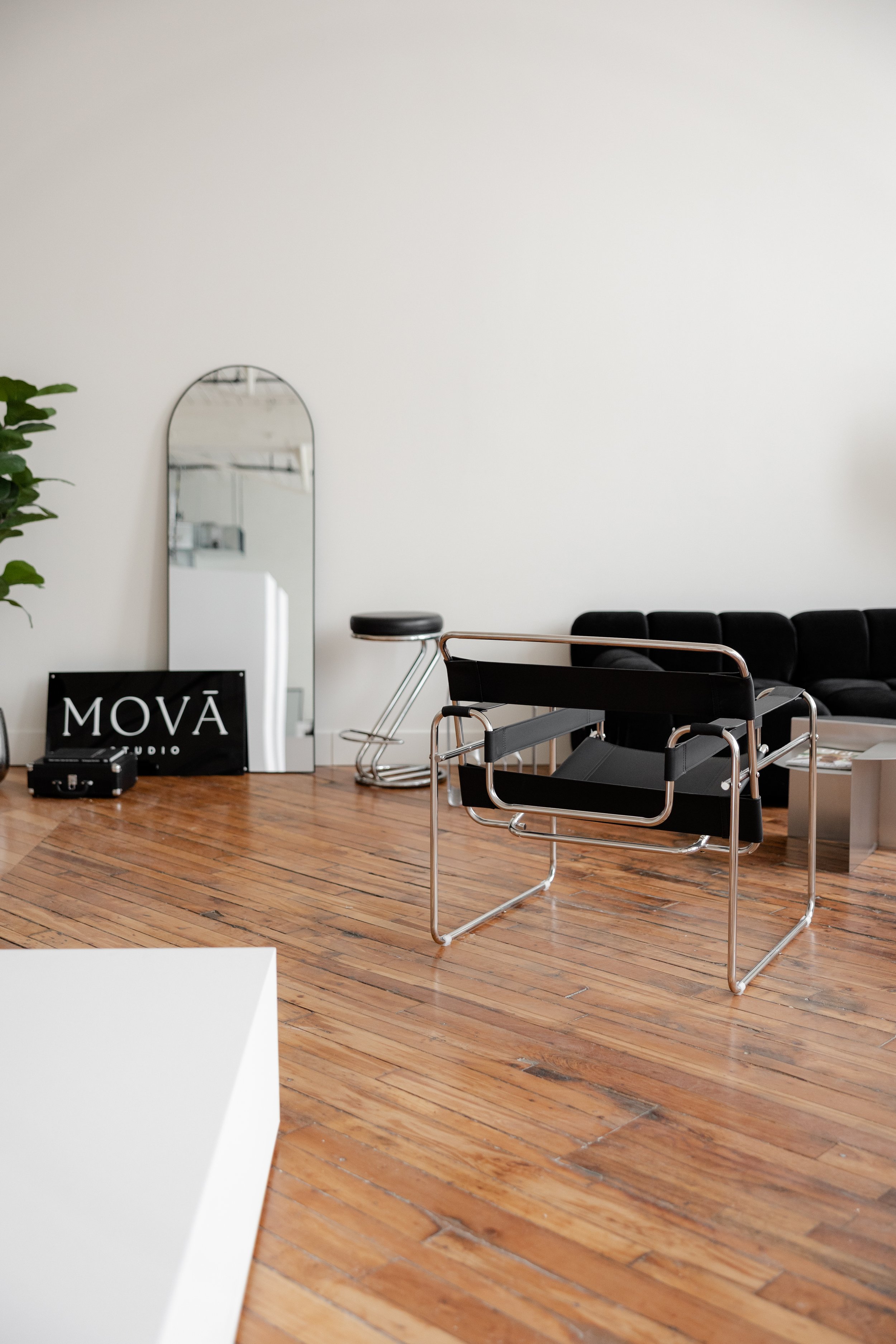 Modern minimalist office or waiting area with a black leather sofa, black Rietveld chair, mirror, and wooden floor.