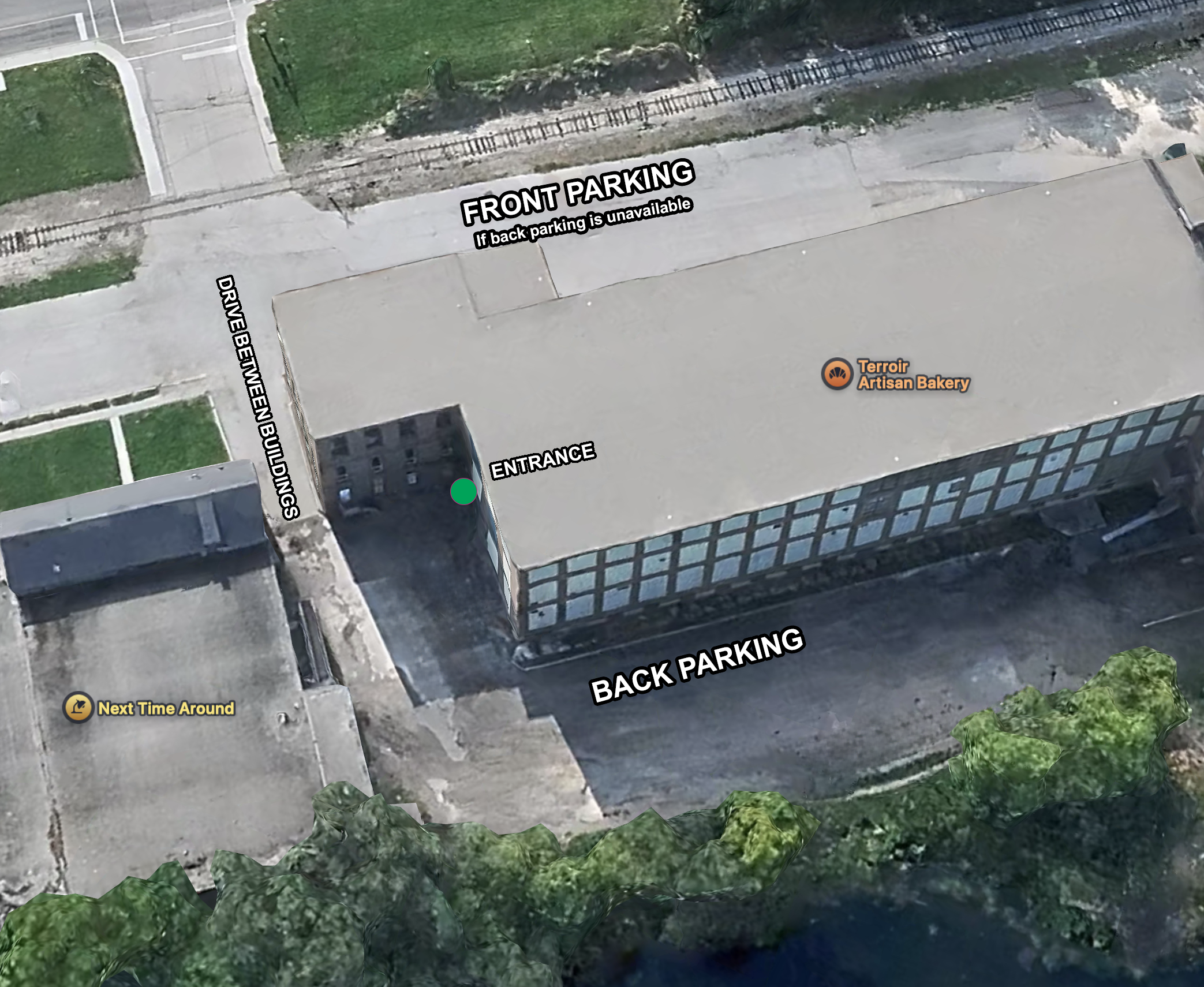Aerial view of a building with labeled entrances, parking areas, and surrounding greenery. The building has front and back parking lots, an entrance at the corner, and a bakery called Terroir Artisan Bakery on the roof. The front parking is unavailable if back parking is free, and there's a drive between buildings.