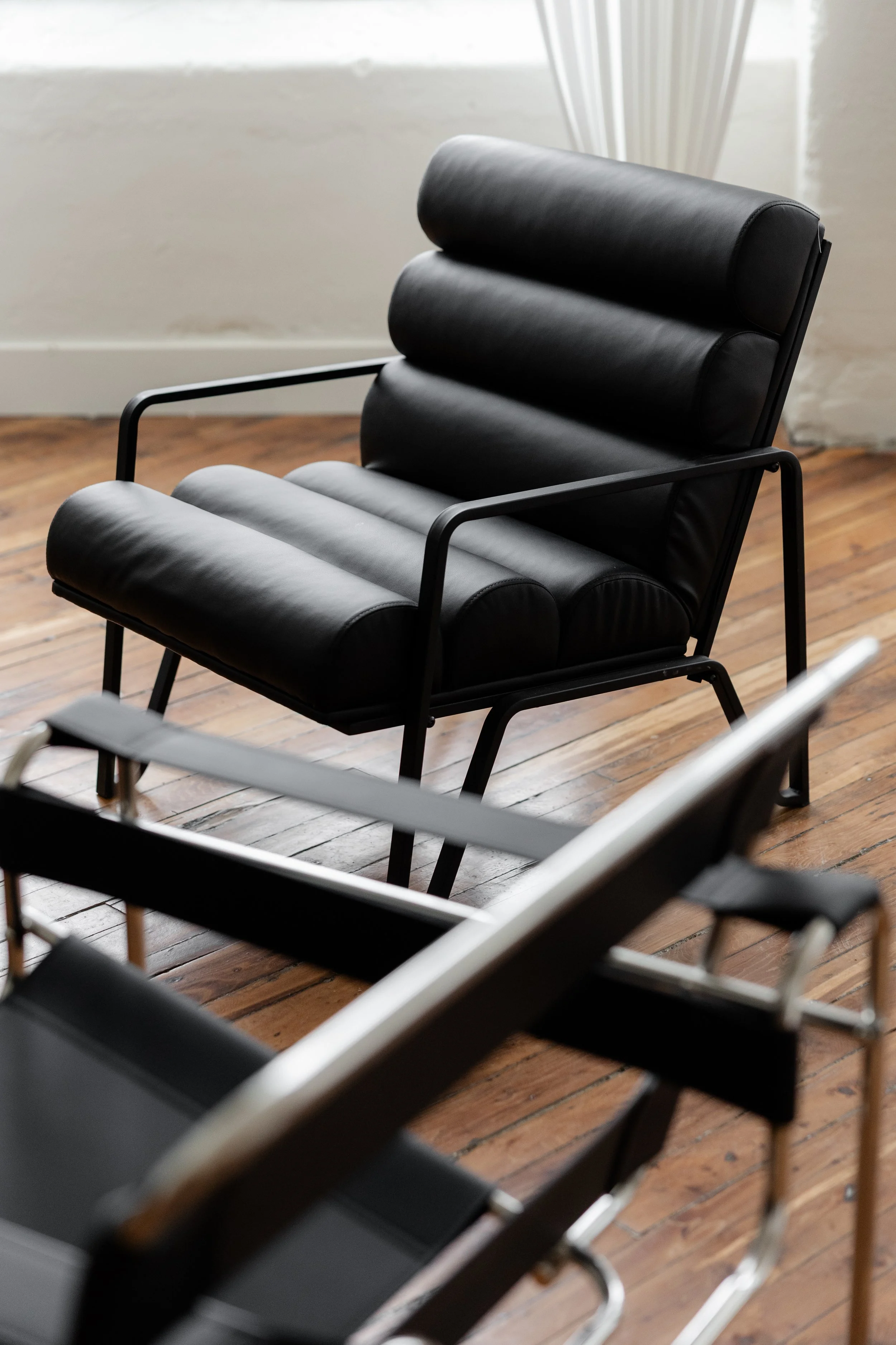 Black modern lounge chairs on a wooden floor in a well-lit room.