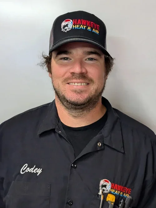 A man wearing a black cap with the Hawkeye Heat & Air logo and and a nametag that says 'Codey'.