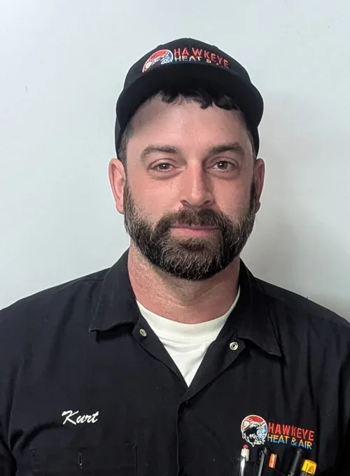 A man with a beard wearing a black cap and black shirt with an embroidered logo of HawkEye Heat & Air. The cap also has the same logo, and the shirt has the name 'Kurt' embroidered on it.