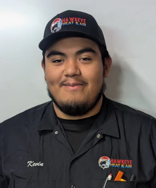 A young man wearing a black cap and black shirt, both with the Hawkeye Heat & Air logo. He has a beard and is smiling against a plain white wall.