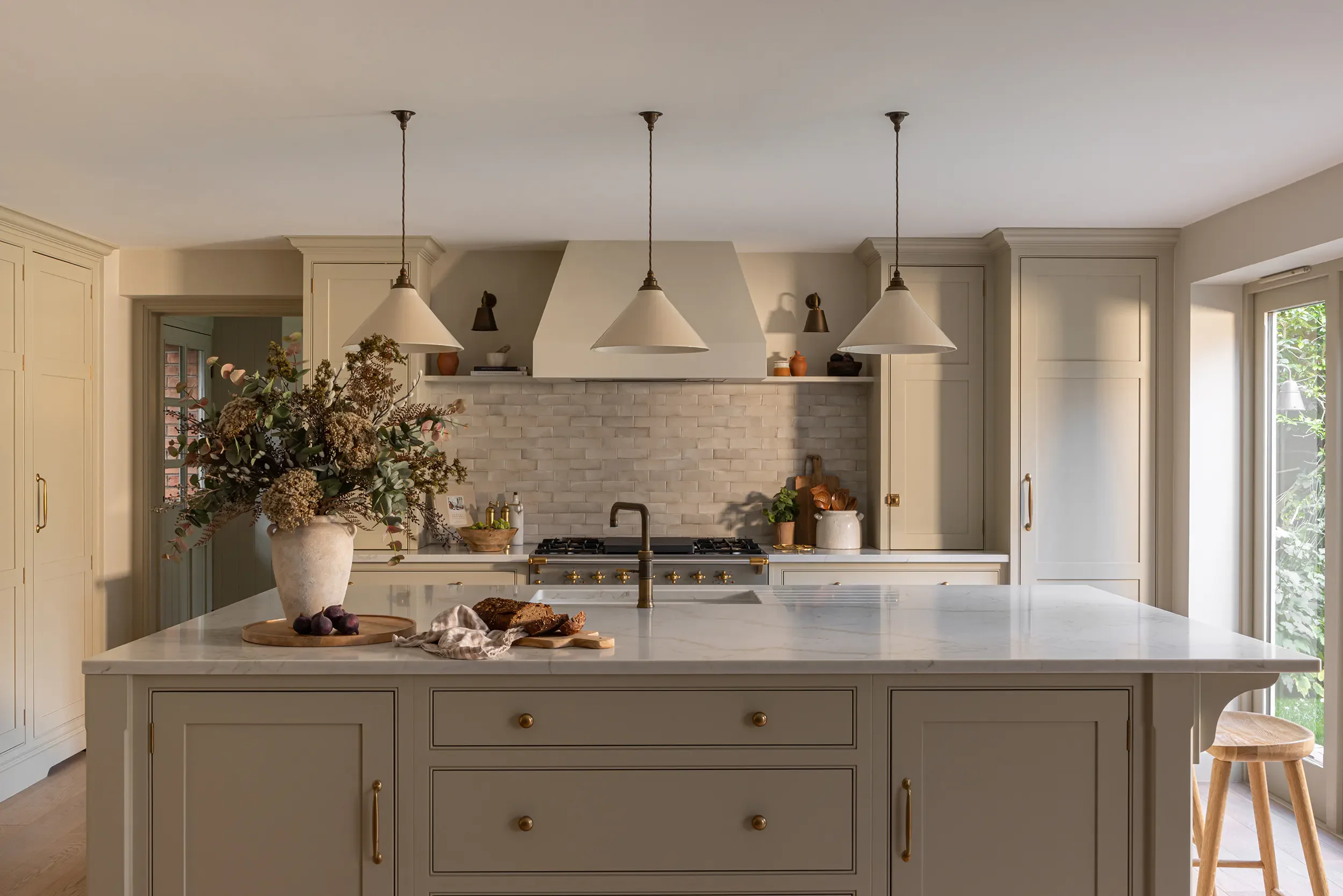 A kitchen with a white marble island, with a brick backsplash and pendant lights overhead.