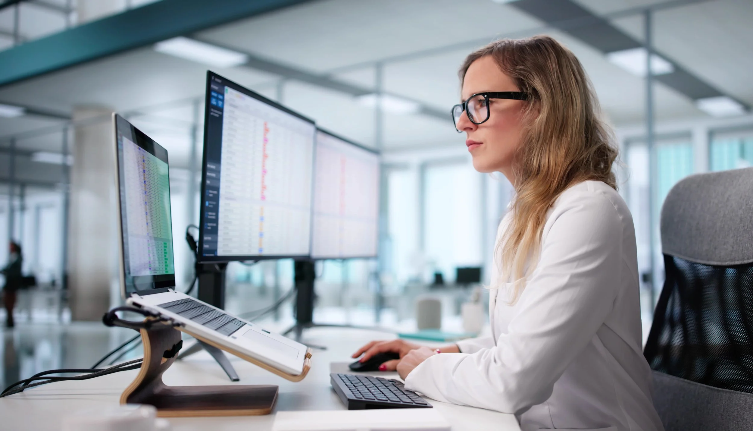 Woman with glasses working on dual computer monitors in an office.