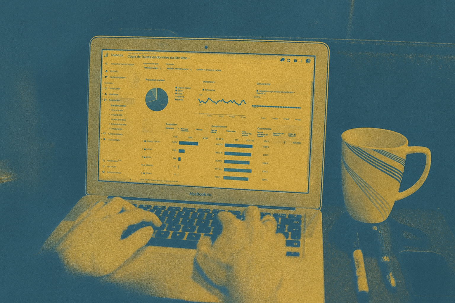 Person using a laptop displaying analytics graphs and charts, seated next to a striped coffee mug on a desk.