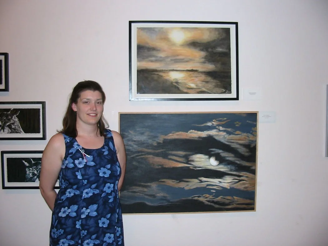 Stacy standing next to her acrylic painting of a moon glowing through dark clouds.