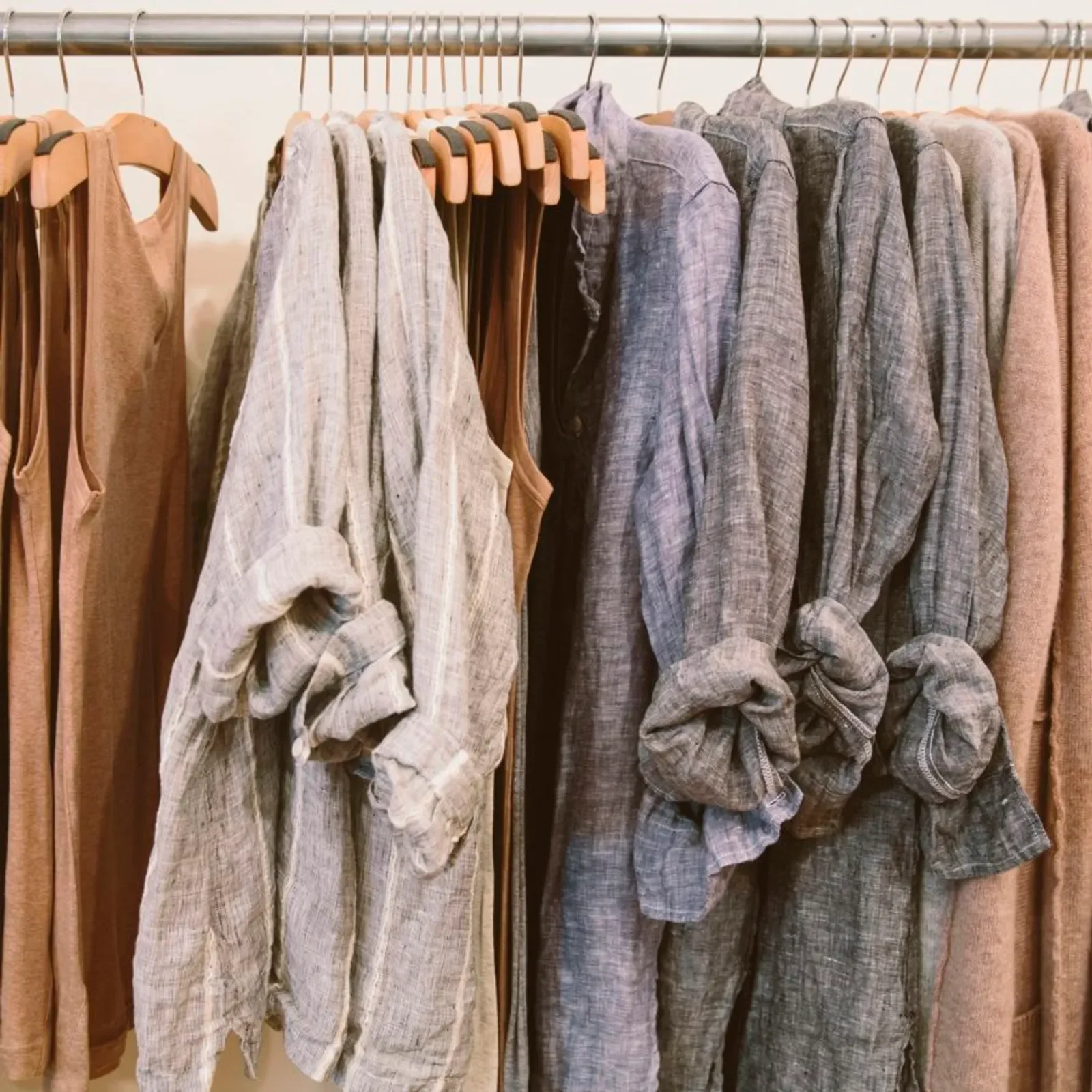 Clothes hanging on a rack, including light-colored shirts and darker long-sleeve shirts or blouses.