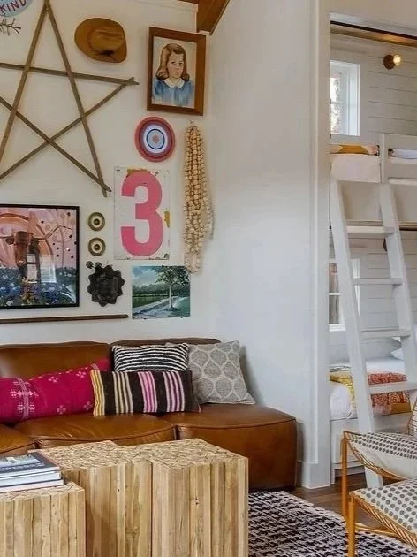 Living room with gallery wall, brown leather sofa with striped pillows, wooden coffee table, and white bunk beds in the background.