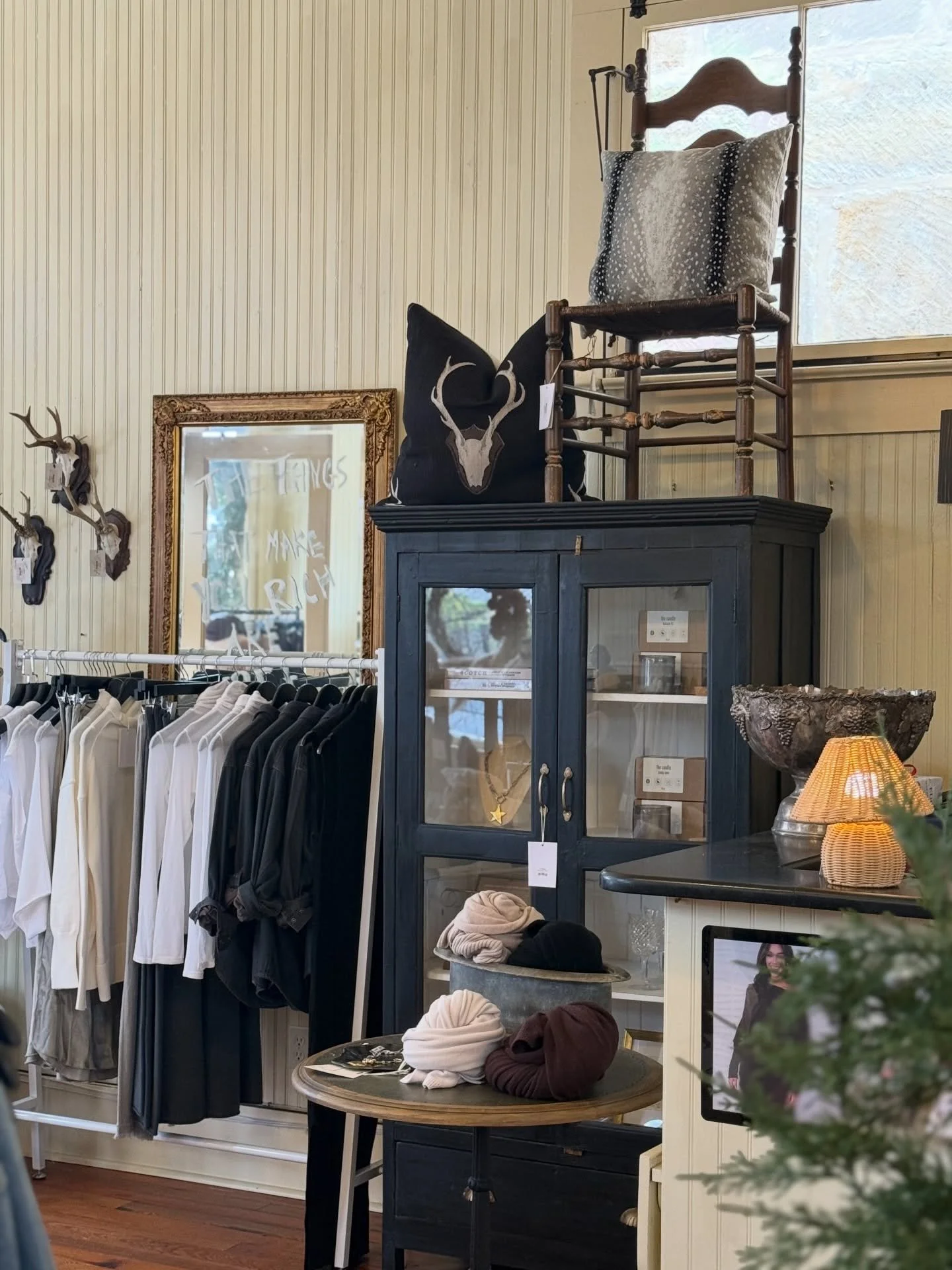 Interior of a shop with clothing racks, a black cabinet, and decorative items like a skull pillow, hats, and antler wall decorations.