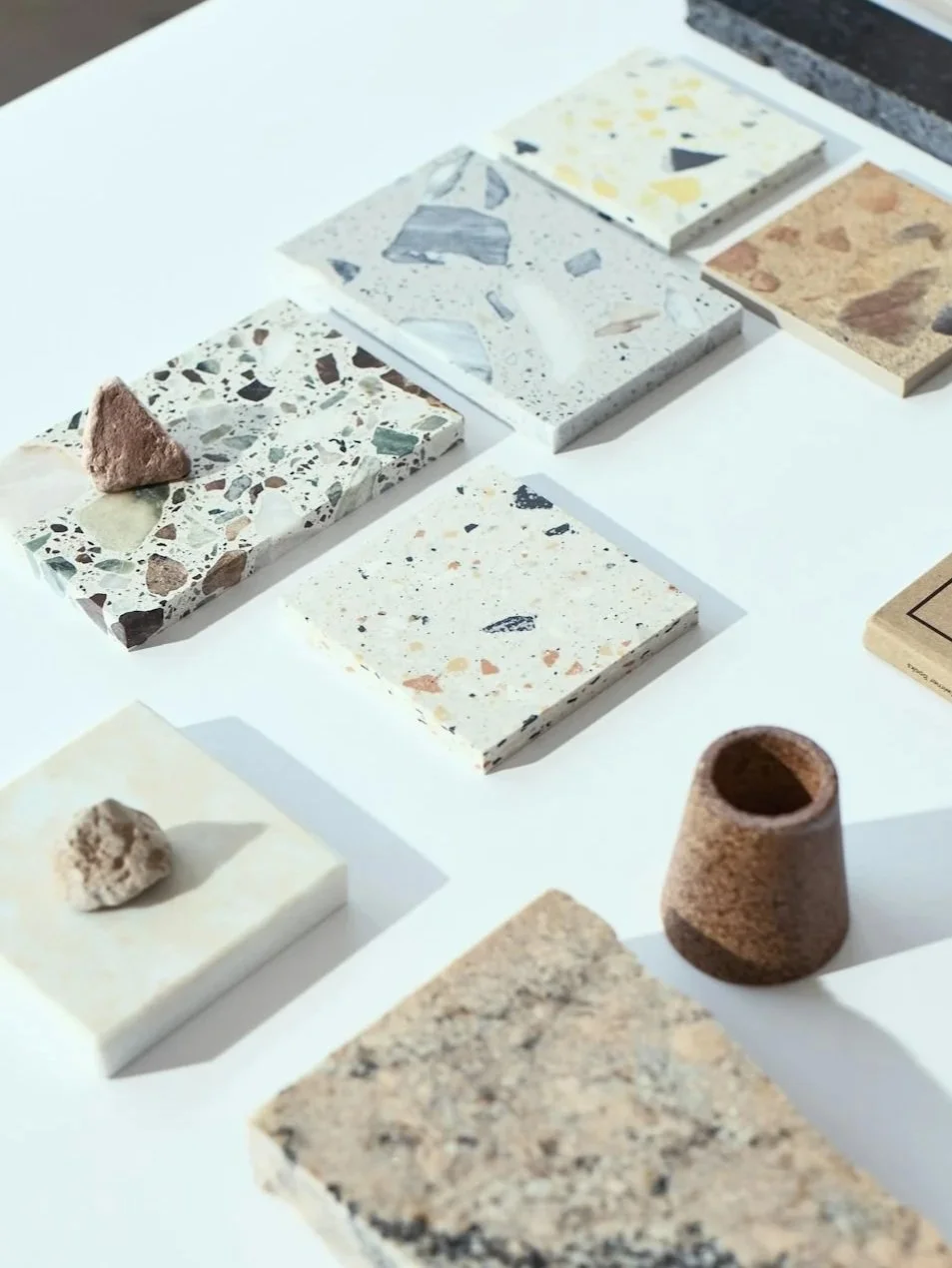Samples of various types of terrazzo and stone tiles displayed on a white surface.