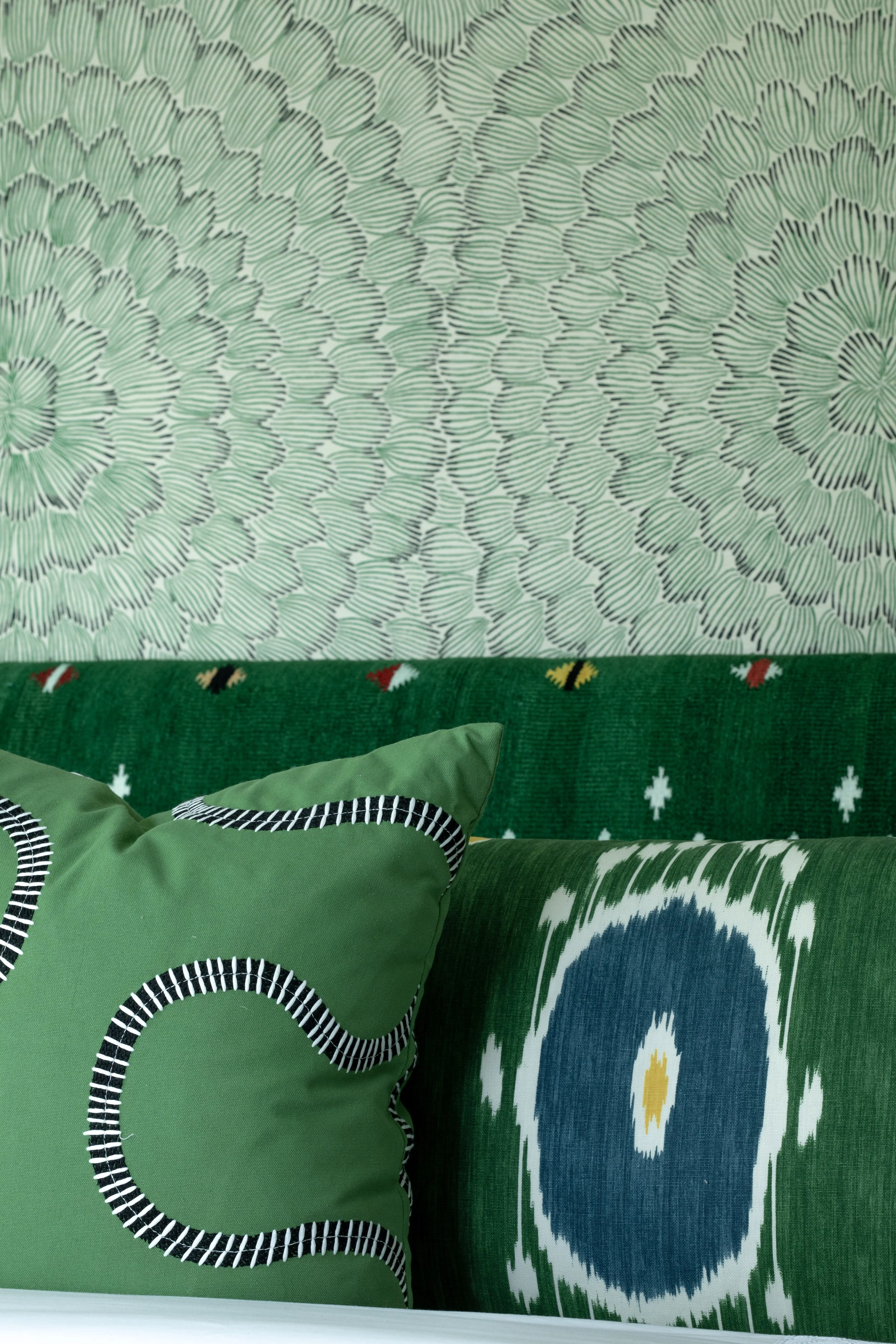 Close-up of green decorative pillows with black, white, and yellow accents on a bed, against a patterned green and white wall.