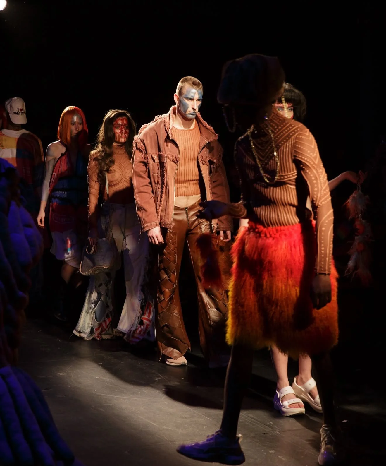 Fashion models walking on a runway during a fashion show, showcasing eclectic and colorful outfits with bold accessories.