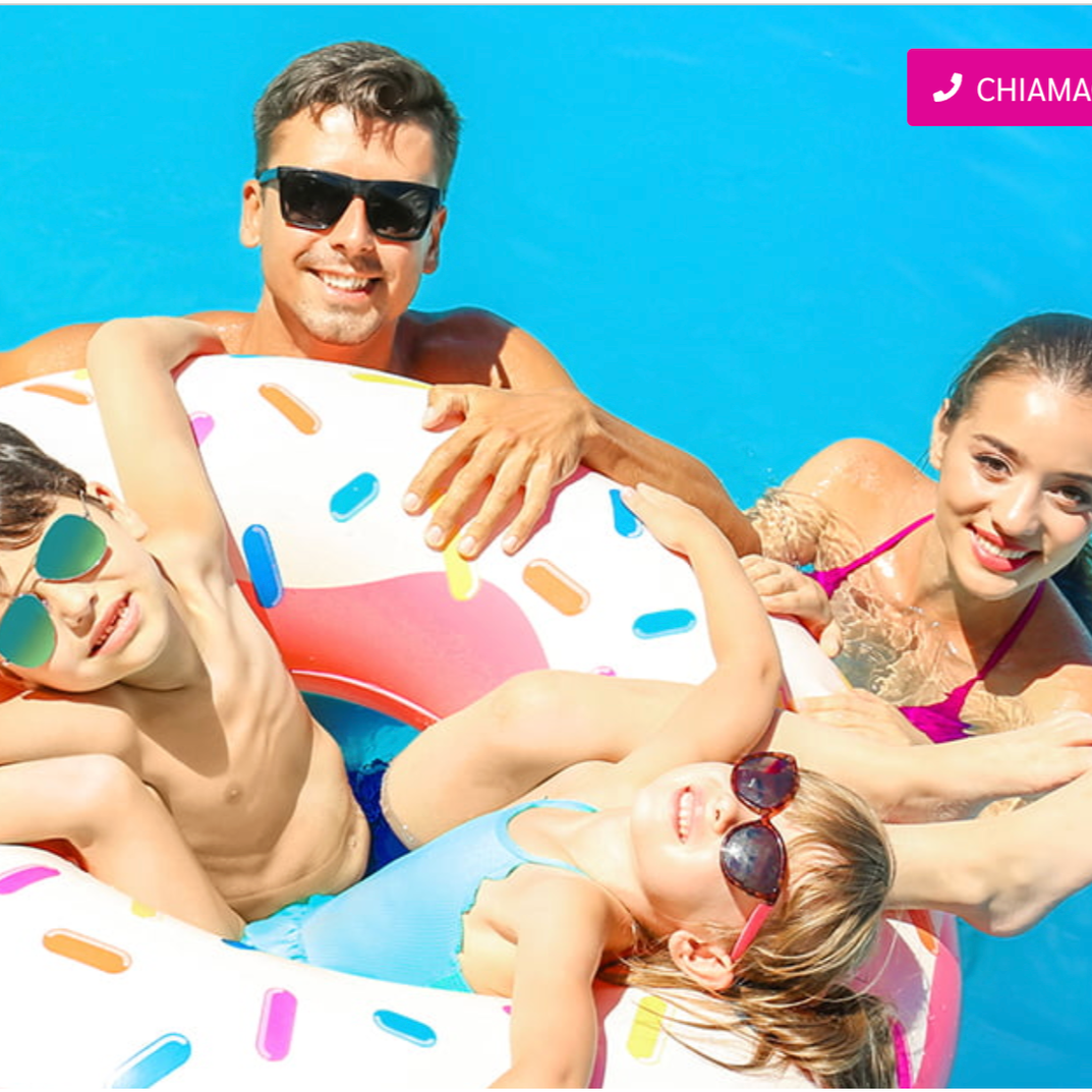 Una famiglia con due bambini nuota in piscina durante una giornata di sole, tutti indossano occhiali da sole e sorridono.