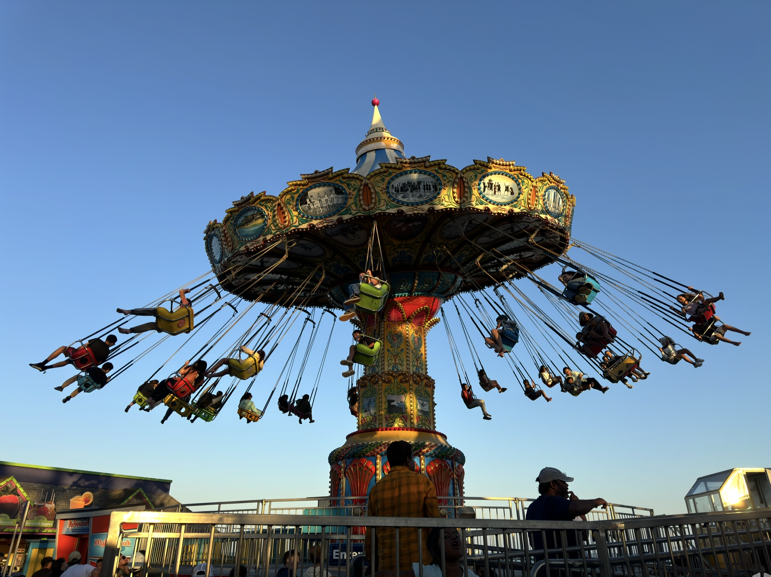 People on a colorful swing ride at Santa Cruz Beach Boardwalk amusement park in Santa Cruz, California during the day with a clear blue sky.