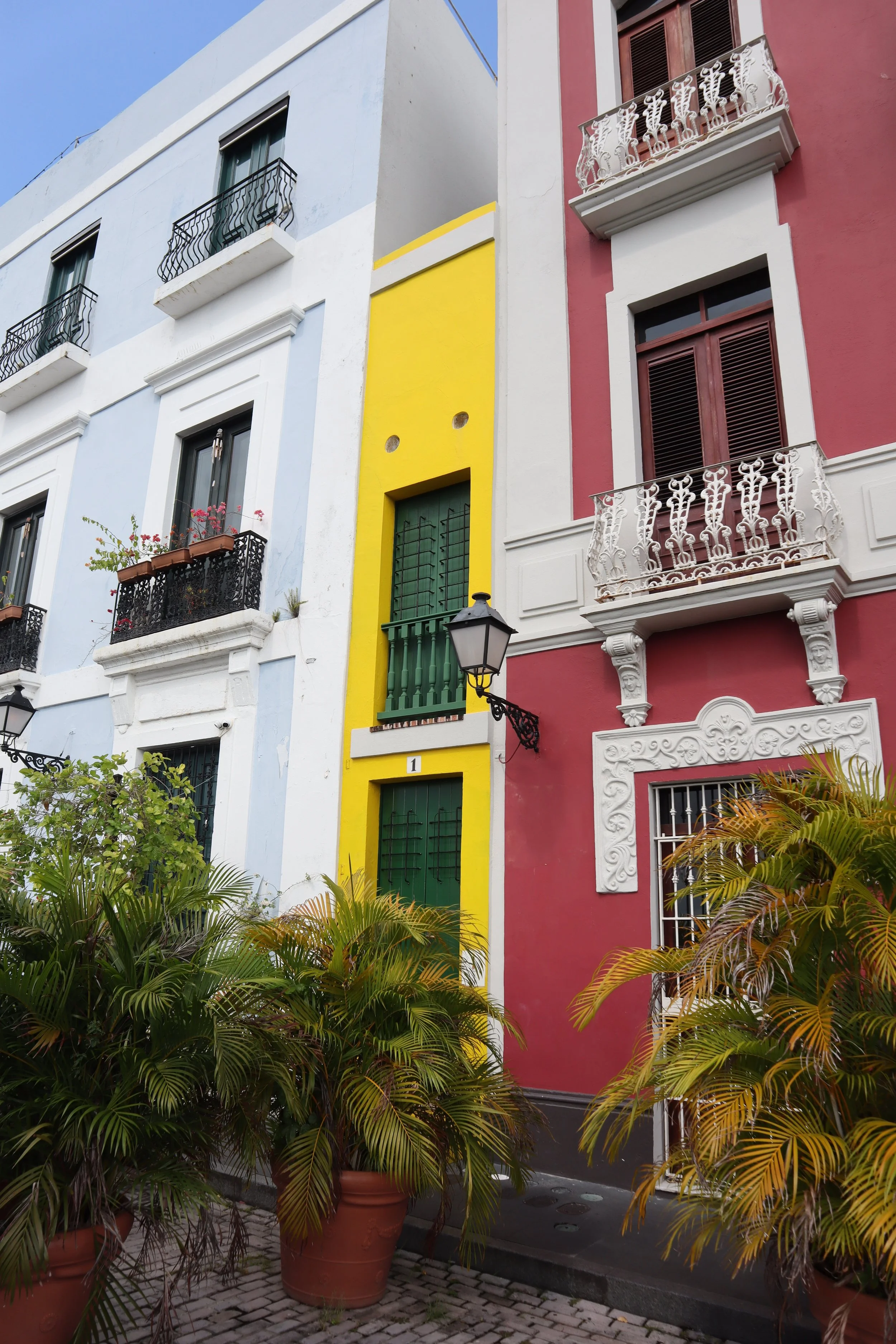 Colorful building facades with balconies and potted plants, featuring blue, yellow, and red walls.