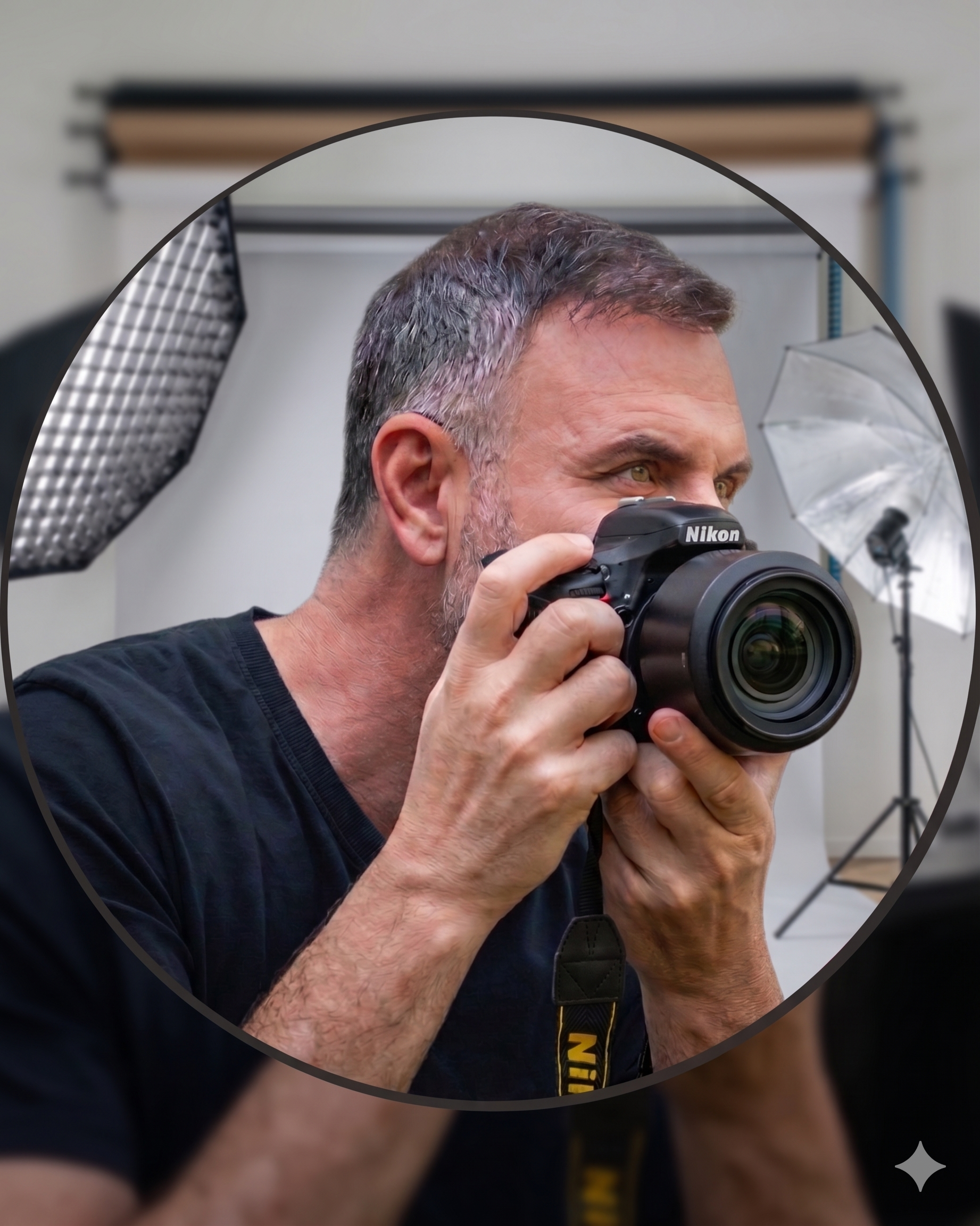 A man with gray hair taking a photo with a Nikon camera in a photography studio with professional lighting equipment and a reflective umbrella.