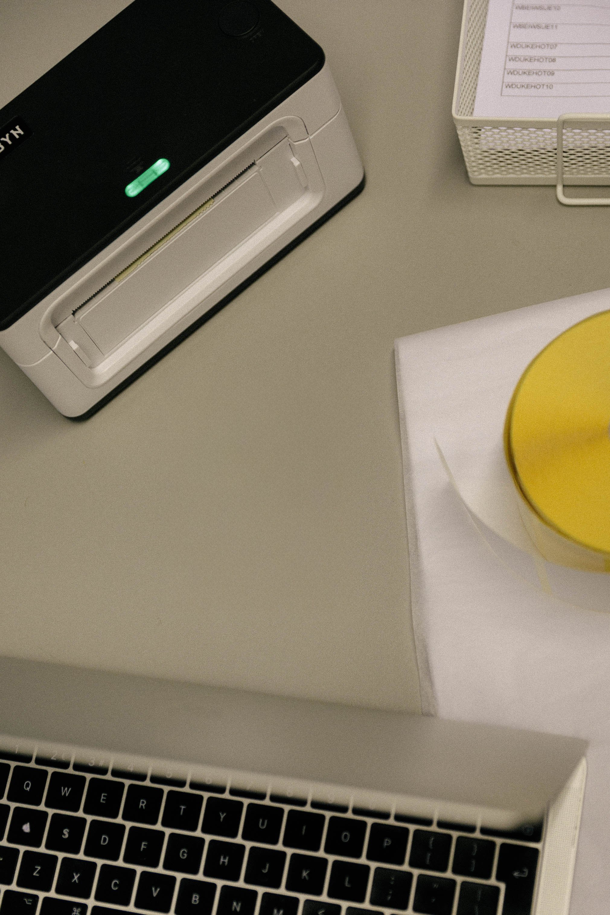 Office desk with a white printer, a notebook with papers, and a partially visible laptop keyboard.