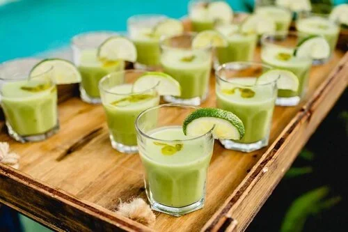 Multiple glasses of green margaritas garnished with lime wedges on a wooden tray.