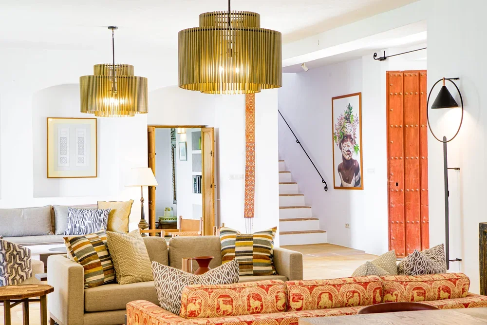 Bright living room with beige and patterned sofas, gold pendant lights, and artwork on white walls.