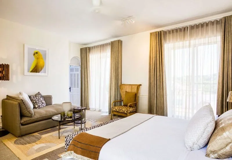 Living room with a bed, sofa, armchair, curtains, and a framed picture of a yellow bird on the wall.