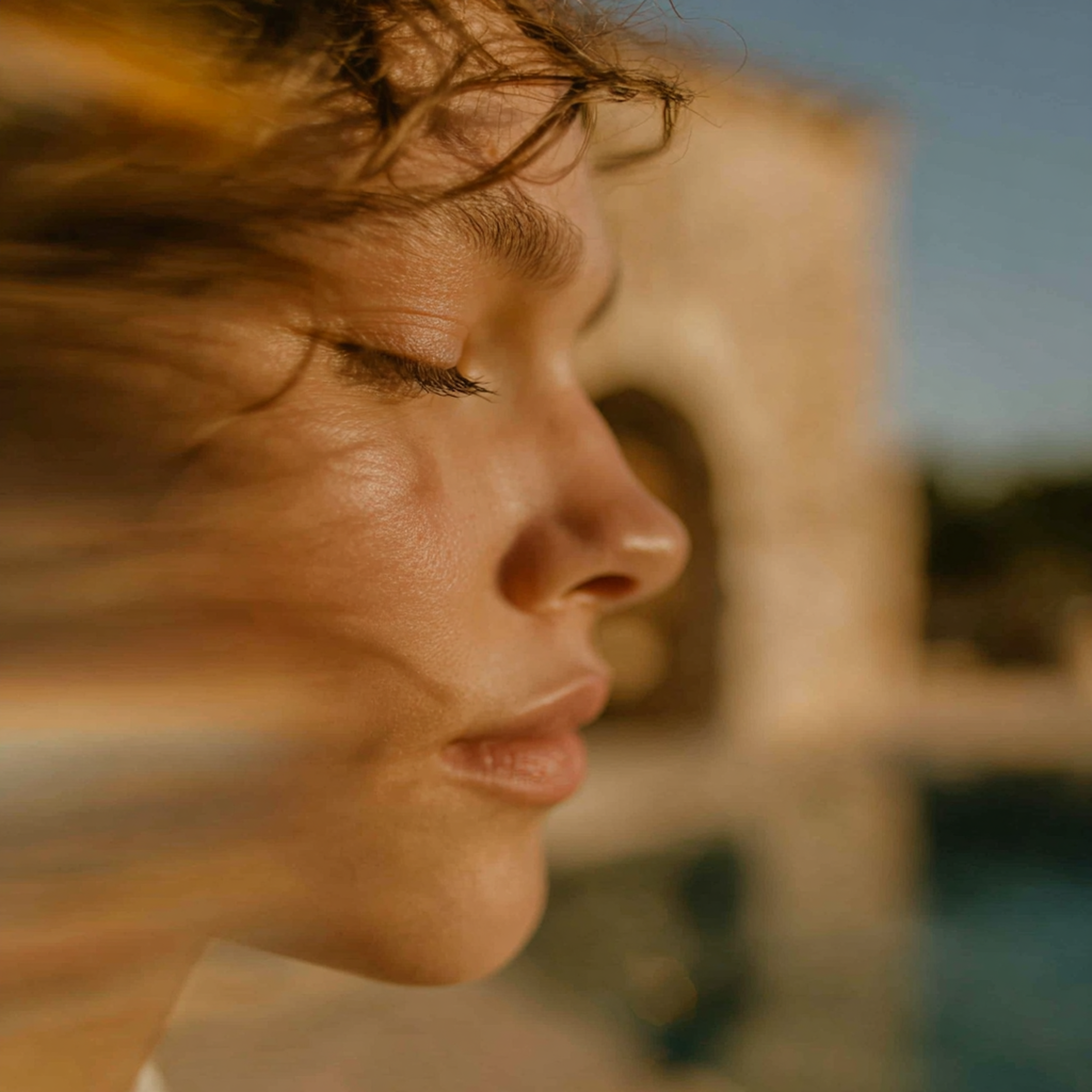 Close-up of a person's face, eyes closed, with wind blowing through their hair.