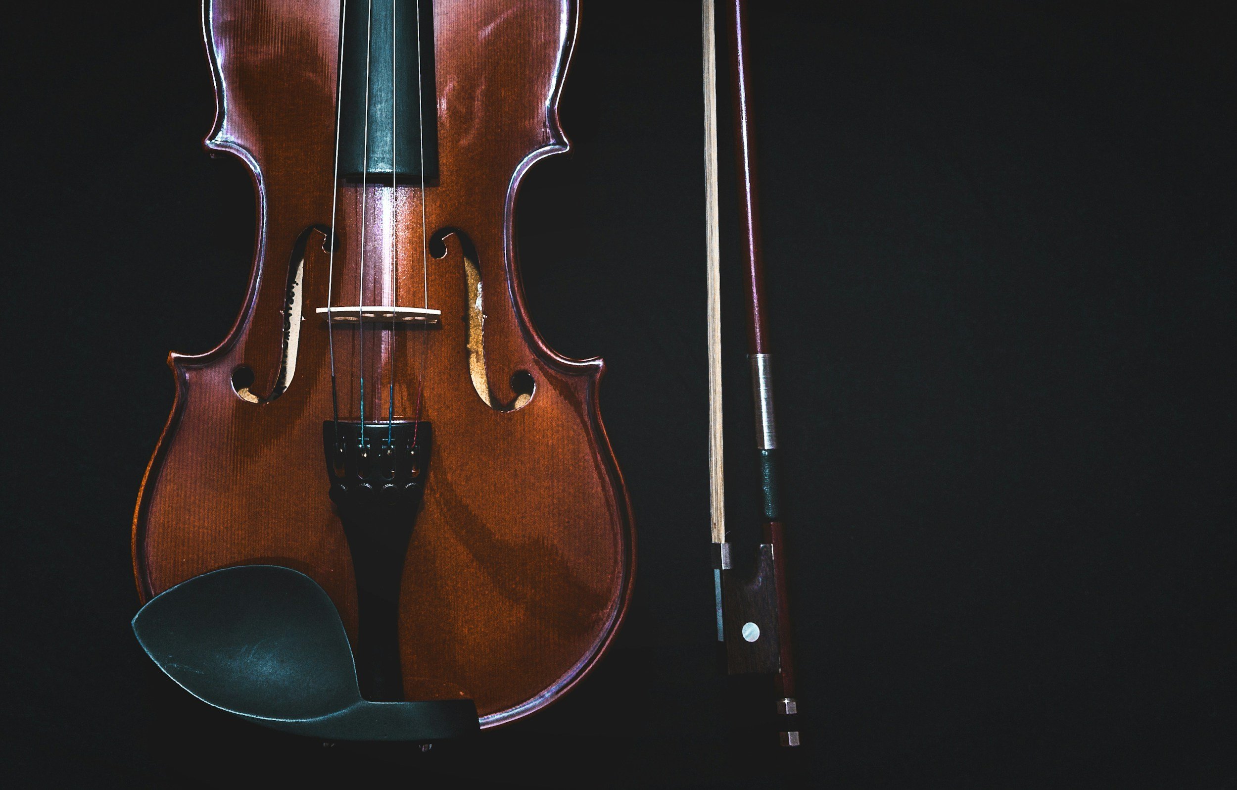 A wooden violin with a bow resting beside it, placed on a black surface.