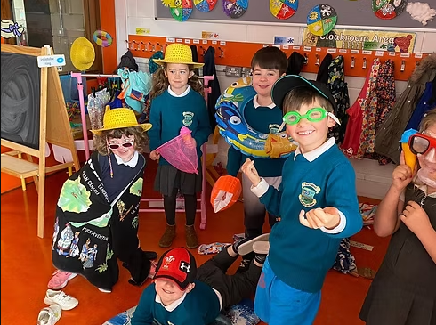 Group of young children dressed in colorful costumes and accessories, including hats, glasses, and scarves, in a classroom with backpacks and colorful artwork on the walls.
