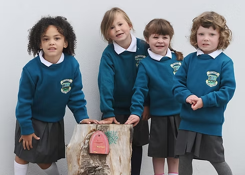 Four young girls in school uniforms standing around a tree stump with a pink toy bag attached to it.