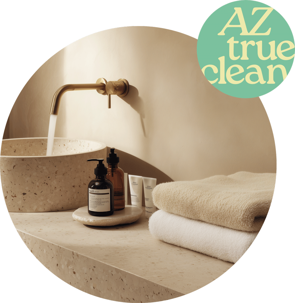 Elegant bathroom vanity with brass wall-mount faucet, terrazzo basin, stacked white towels, and amber bottle amenities with AZ True Clean logo, showcasing vacation rental staging details