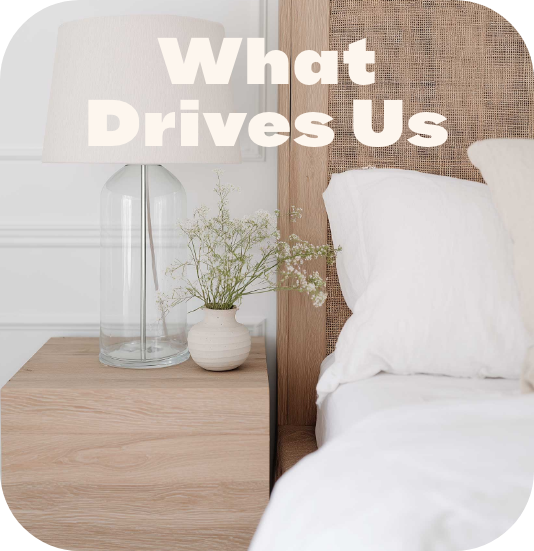 Minimalist bedroom nightstand with fresh flowers in glass vase and wooden cane headboard with text What Drives Us, showcasing design-conscious cleaning approach