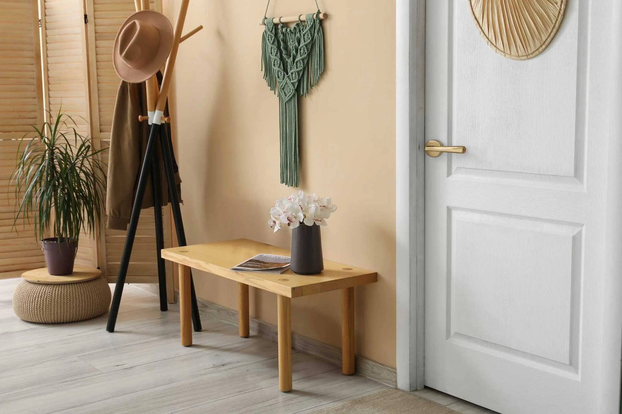 Entryway with coat rack, decorative plant, and a small wooden table with flowers and magazine.