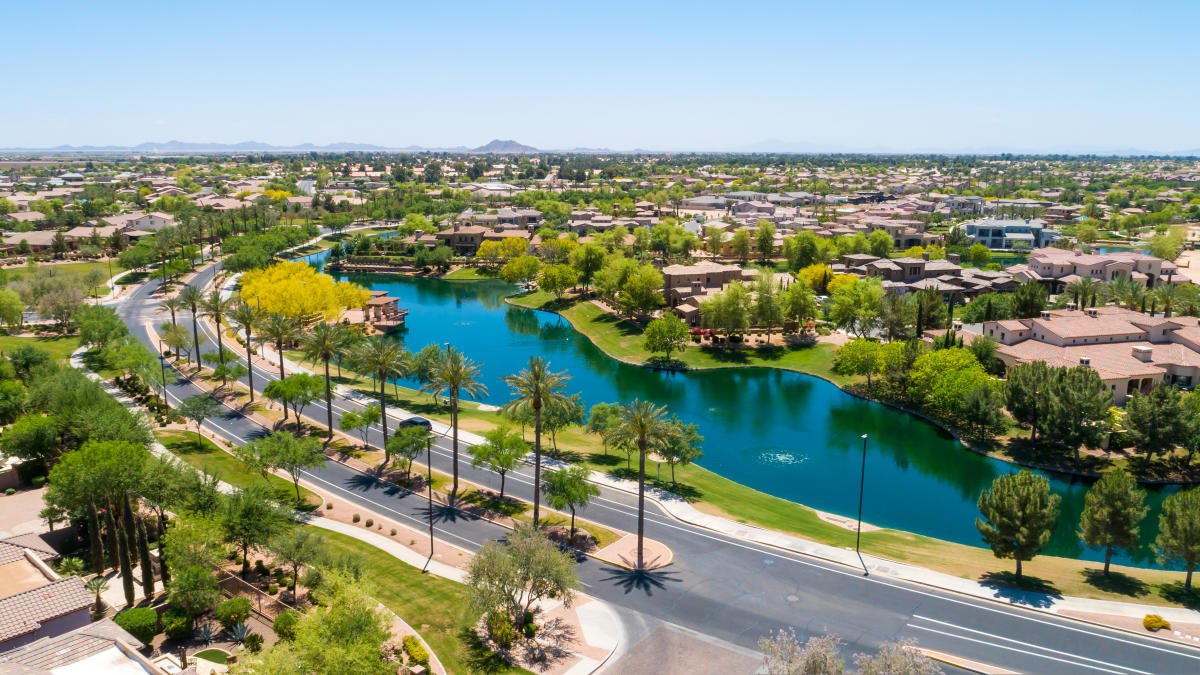 Aerial view of a suburban residential neighborhood with a winding river, trees, and houses under a clear blue sky.