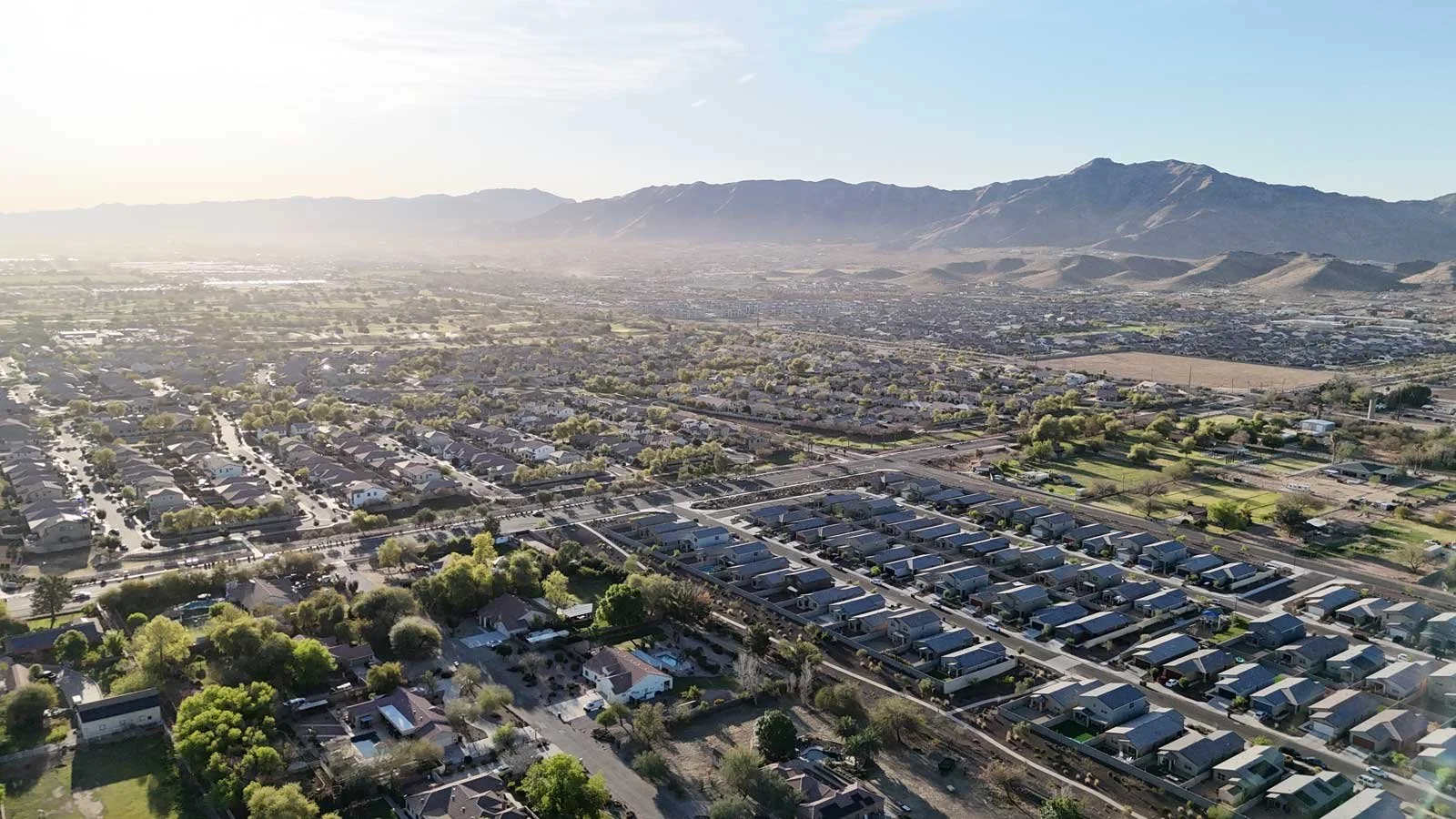 Aerial view of a suburban neighborhood with houses, trees, and streets, with mountains in the background under a clear sky.