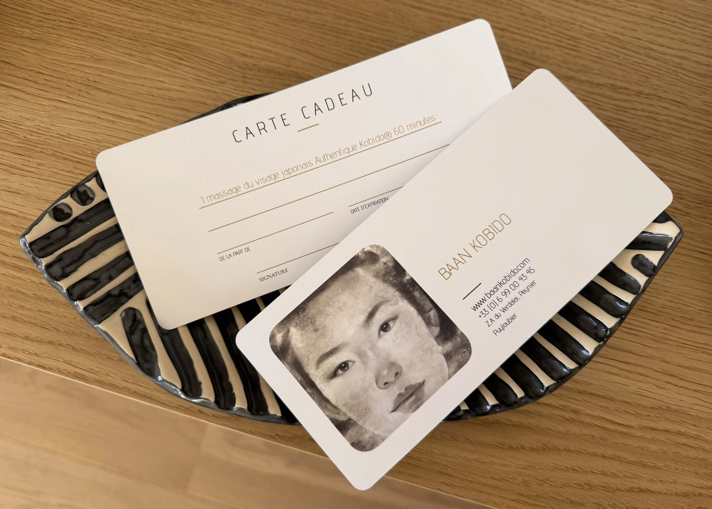 Une carte cadeau recto-verso sur un plateau en céramique noir et blanc posé sur une surface en bois.