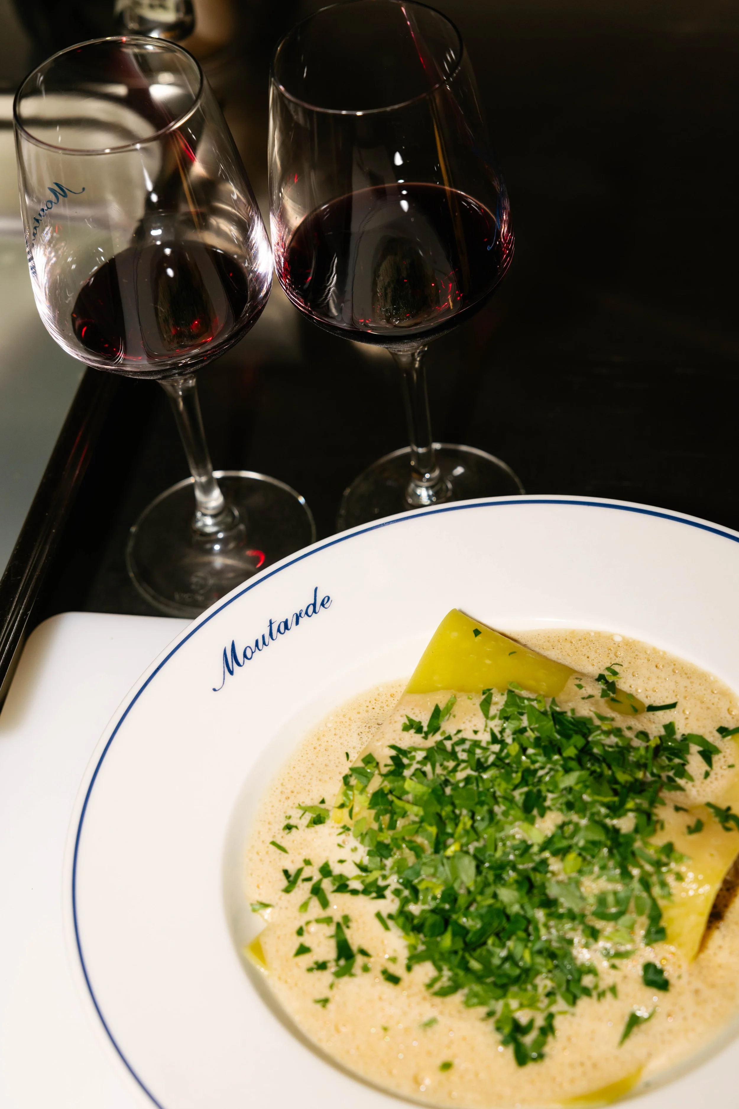 Deux verres de vin rouge à côté d'une assiette de moules à la crème garnies de persil, sur une table sombre.