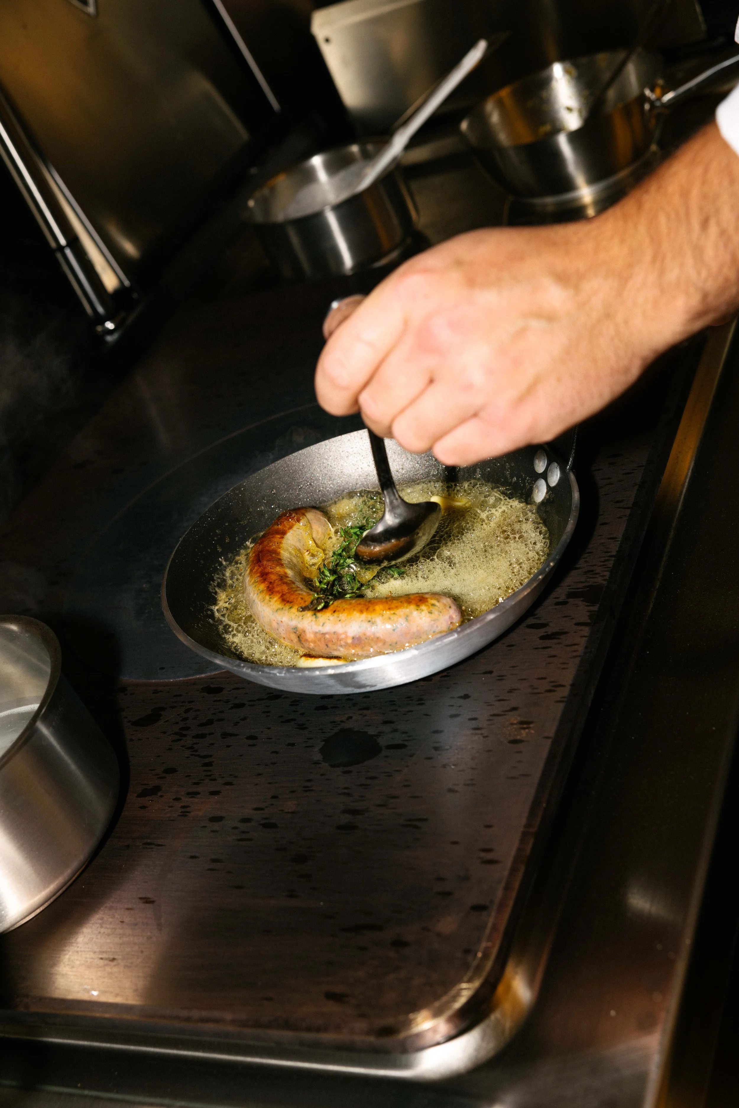 Une main qui cuisine une saucisse dans une poêle avec des herbes et du beurre ou une huile