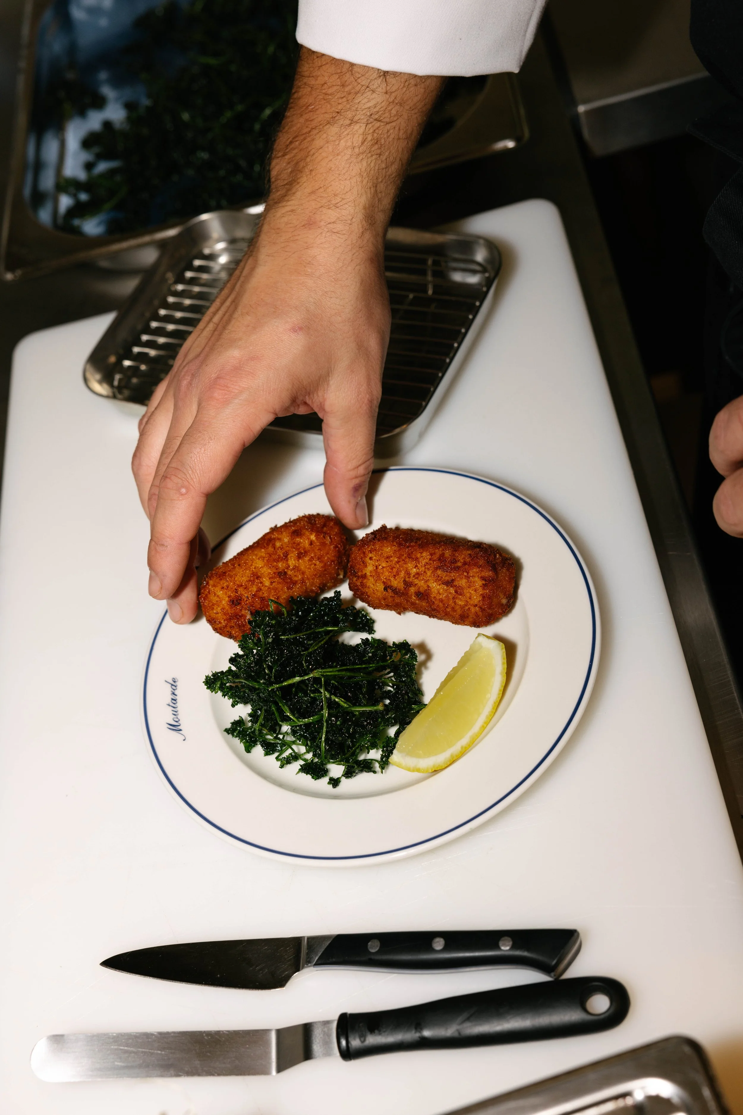 Une assiette avec deux croquettes, une portion de kale sautée, une tranche de citron, et une main positionnée à côté de l'assiette.