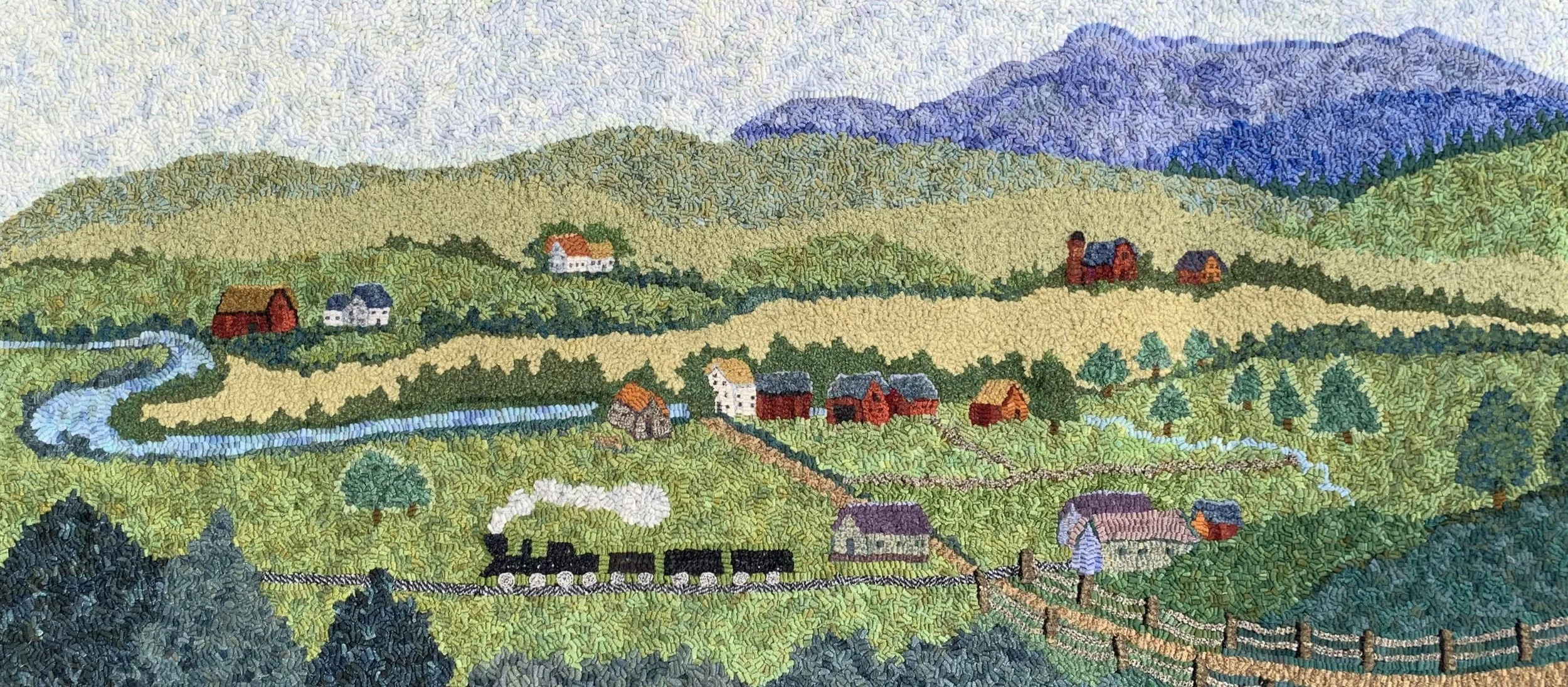 Colorful landscape embroidery depicting rolling green hills, a winding river, small houses, trees, a train, and purple mountains in the background.