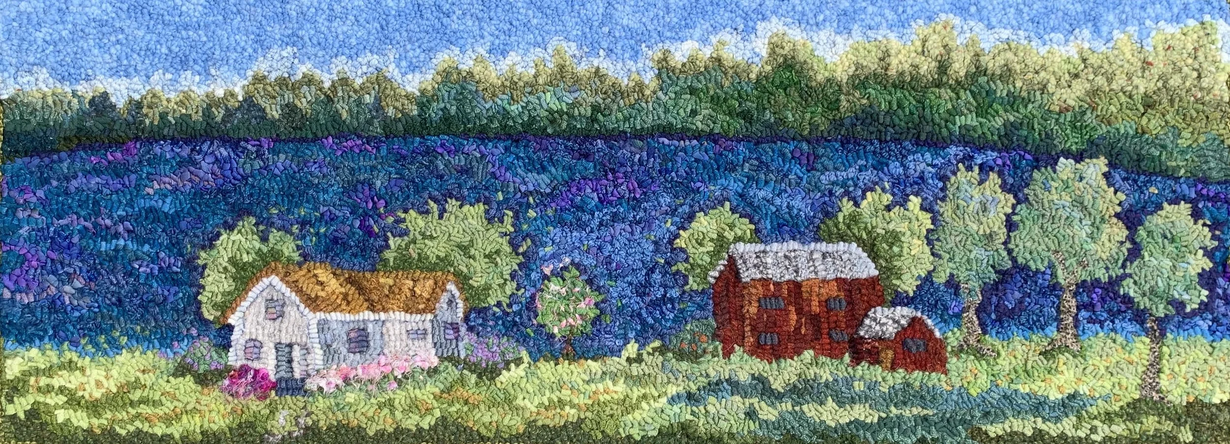 A pixelated embroidery artwork depicting a countryside scene with houses, trees, and a blue sky.
