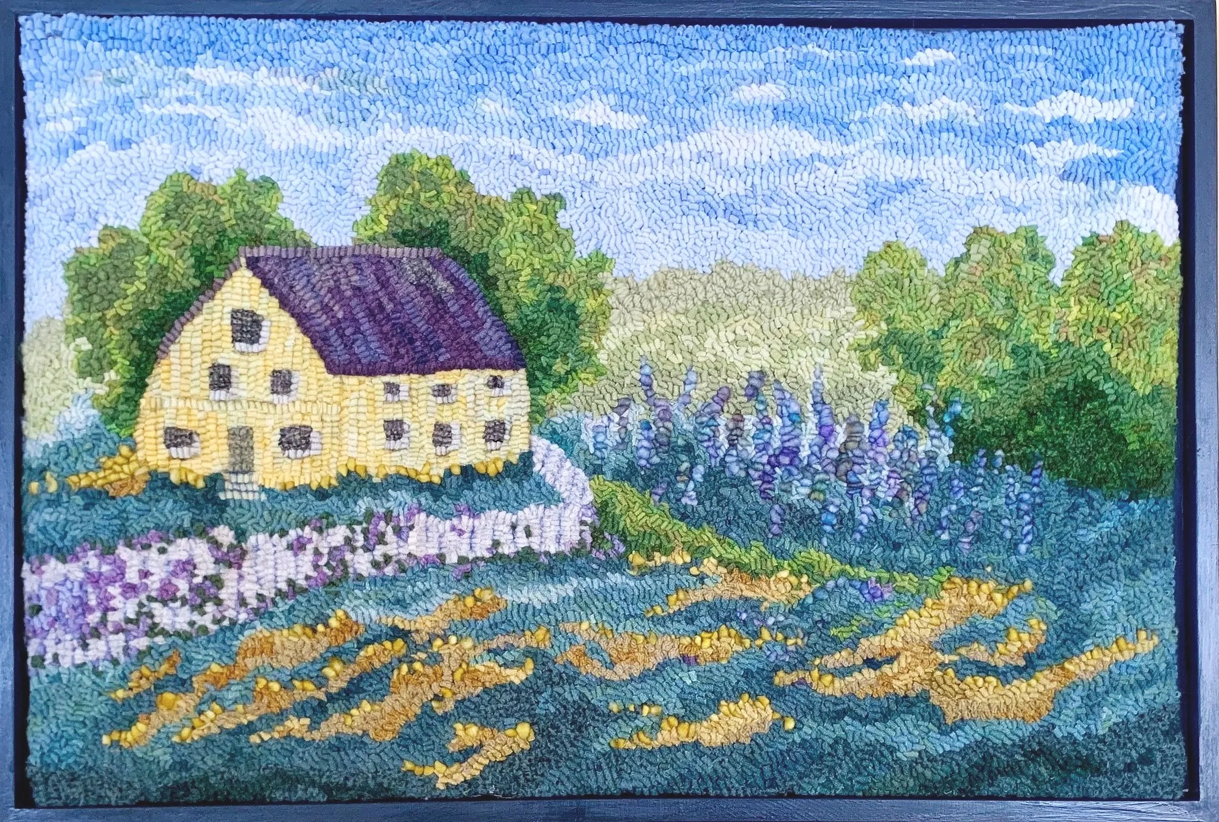 A colorful mosaic artwork depicting a yellow house with a purple roof, surrounded by trees, lavender fields, and blooming flowers under a blue sky with scattered clouds.