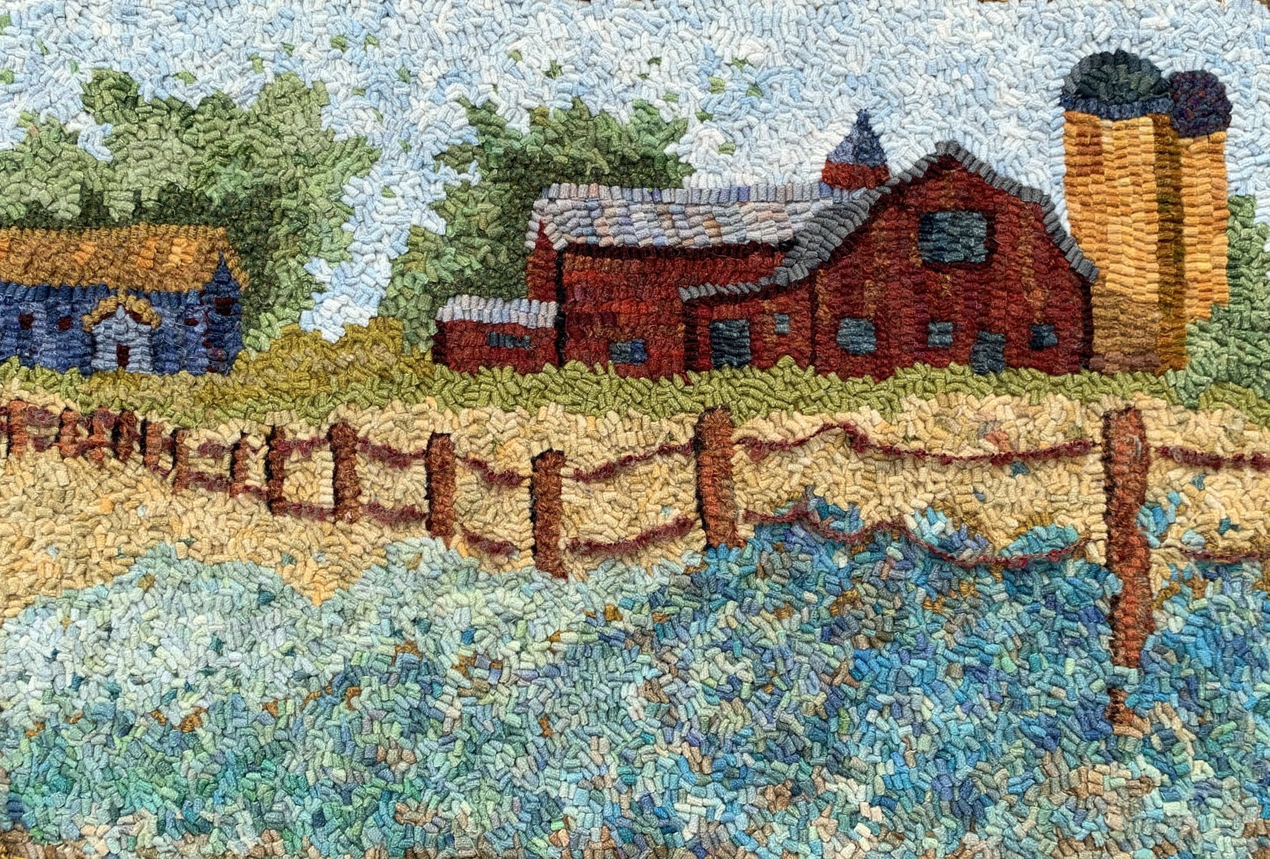 Colorful embroidery of a rural farm scene with red barns, a blue house, a silo, trees, a yellow field, and a fence.