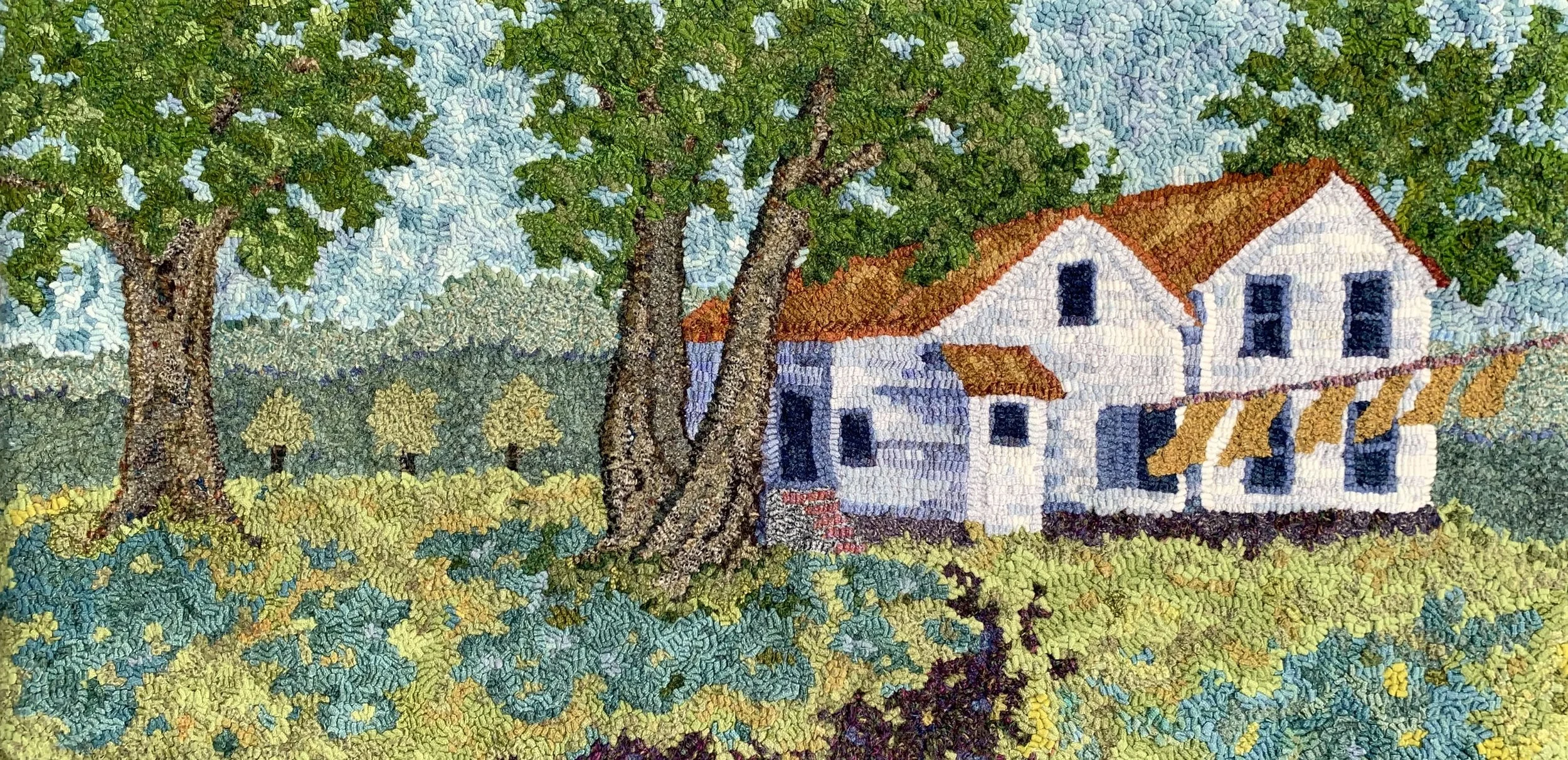 A detailed needlepoint tapestry of a countryside scene featuring large trees, a white house with a red roof, and rolling green fields under a blue sky.