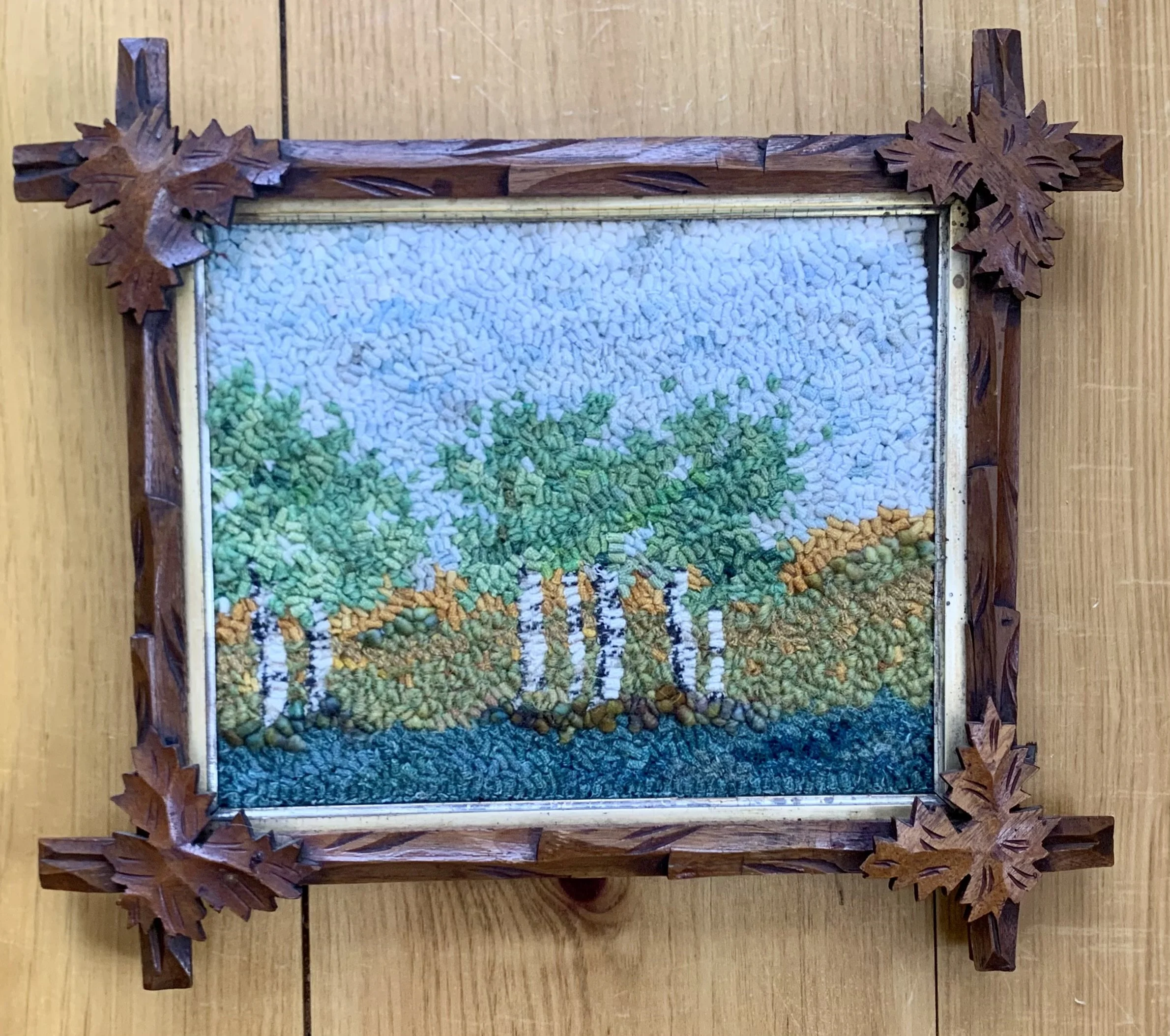 Landscape scene with white birch trees, hand hooked inside a  n antiquewooden frame with carved maple leaf details.