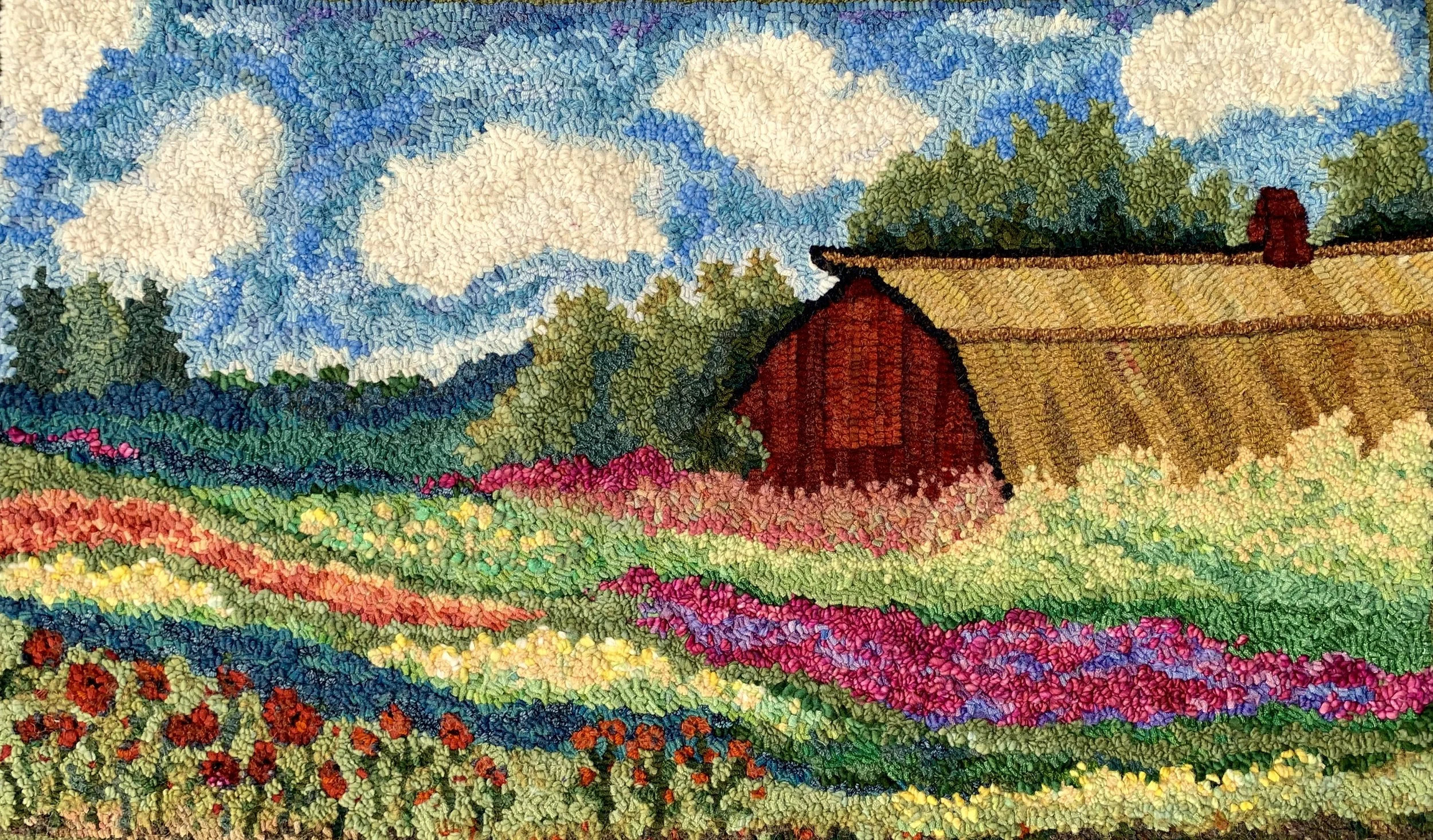 A textured colorful embroidery depicting a rural landscape with a red barn, rolling hills, vibrant flowers, and a partly cloudy sky.