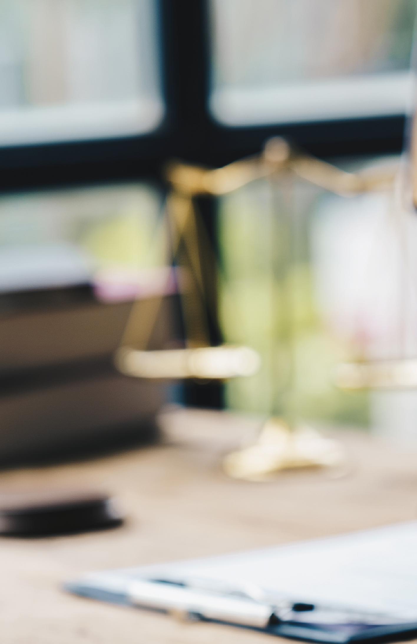 Mesa de oficina con computadora, cuaderno y pluma, en un ambiente con ventana de fondo.