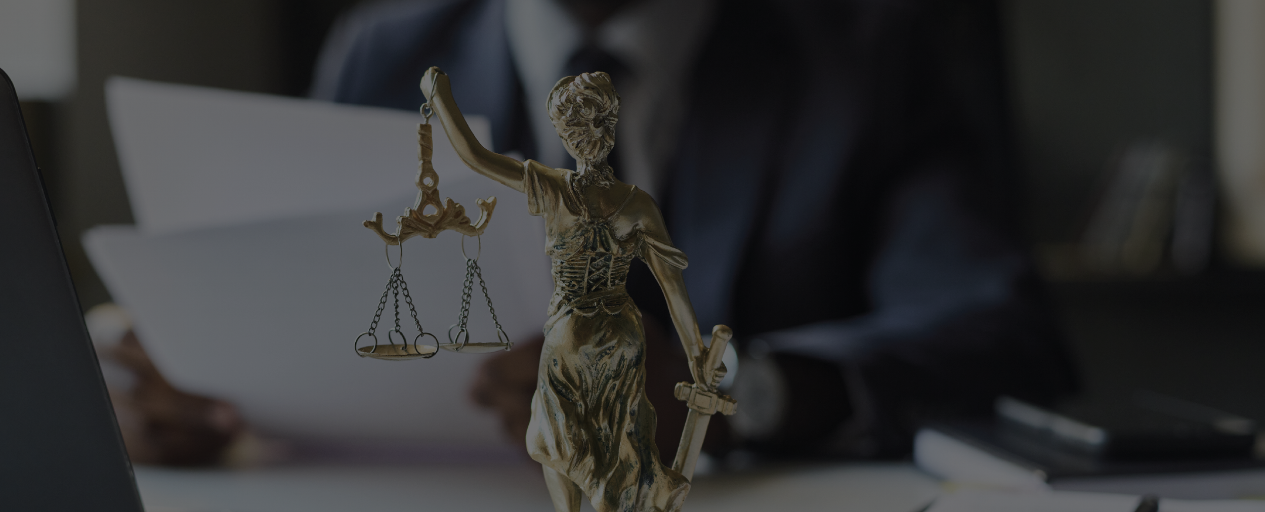 Estatua de la justicia con balanza y espada, en oficina con documentos y persona en el fondo