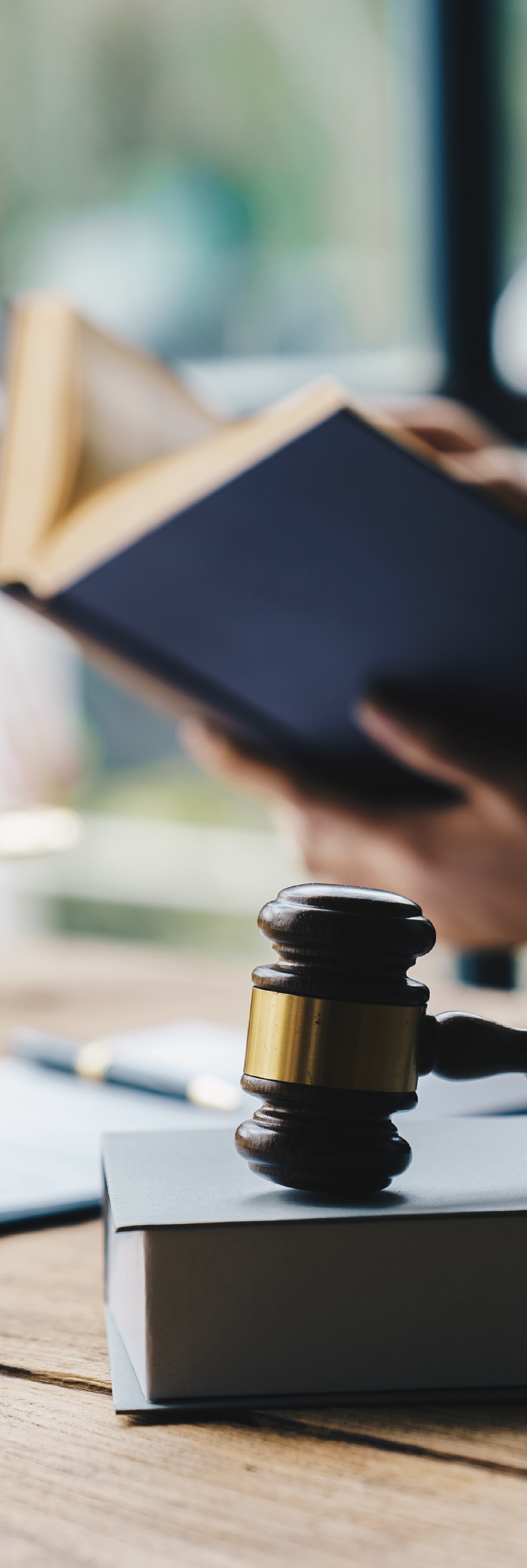 Martillo de juez sobre un libro en una mesa de madera, con una mano tomando un libro en el fondo.