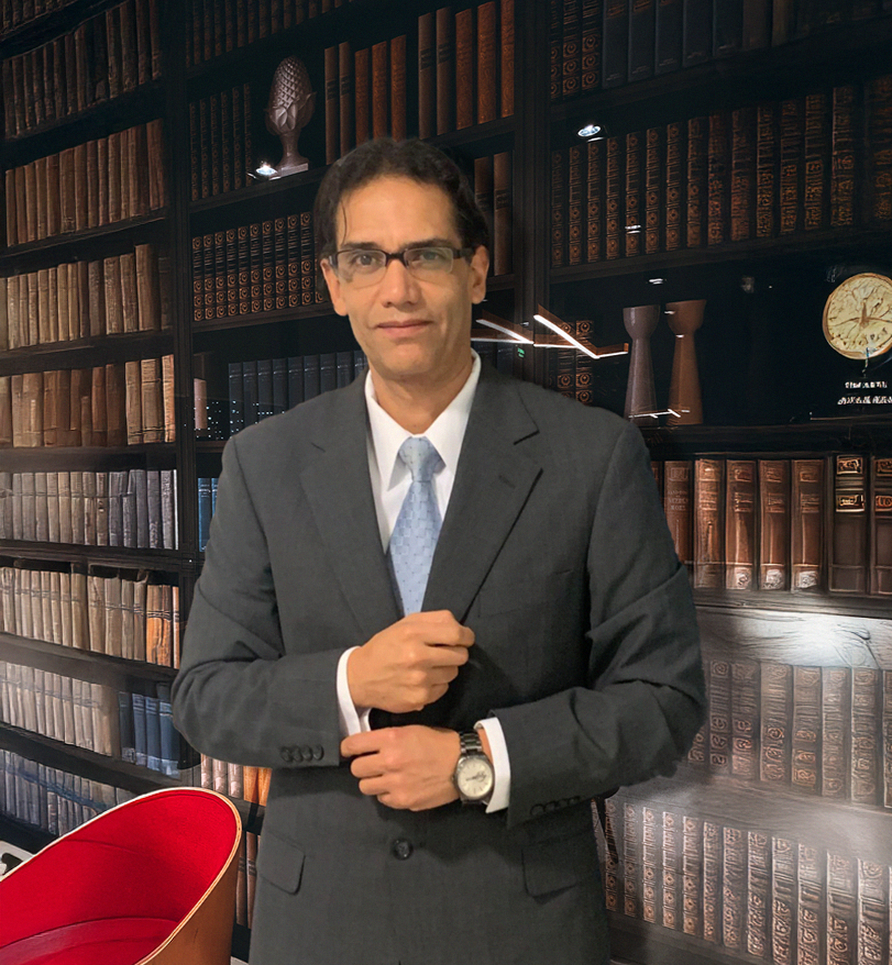 Hombre con gafas y traje gris en una biblioteca con estanterías llenas de libros antiguos.