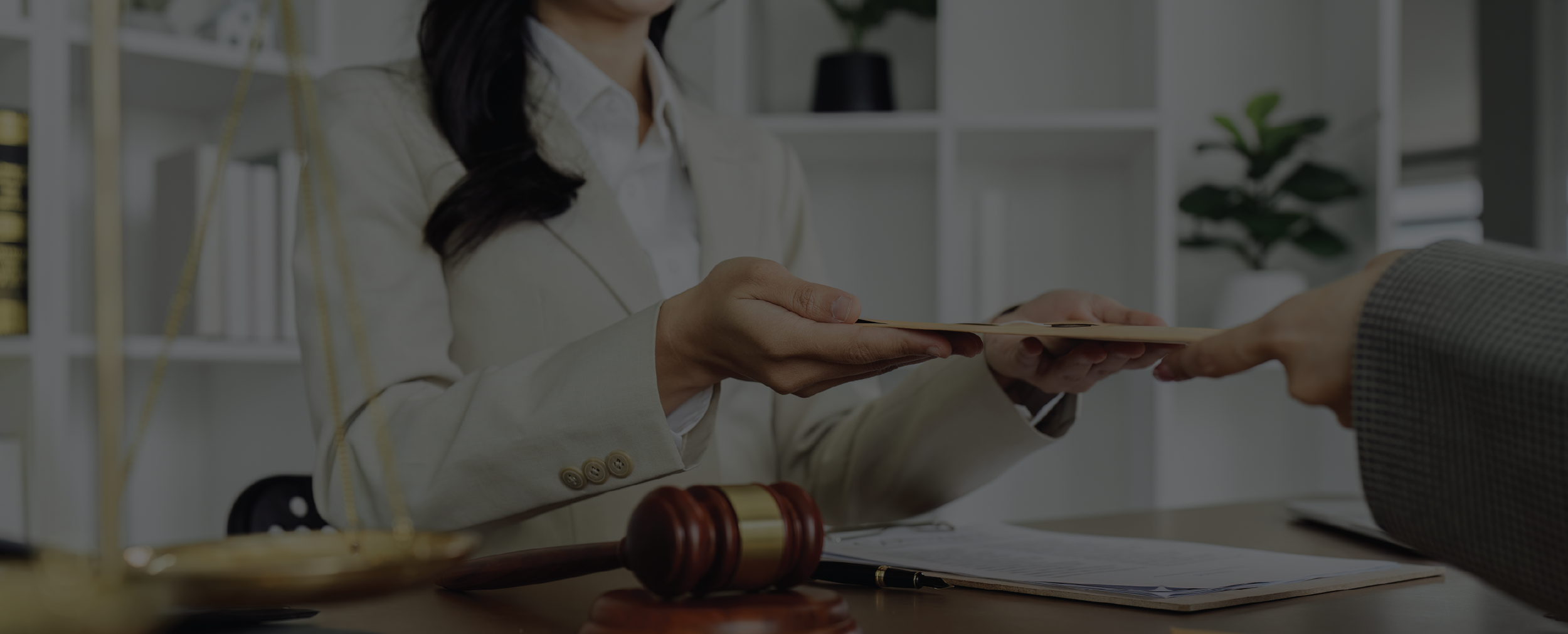 Una mujer en un entorno de oficina entregando un expediente a otra persona, con una balanza y un mazo de juez en primer plano.